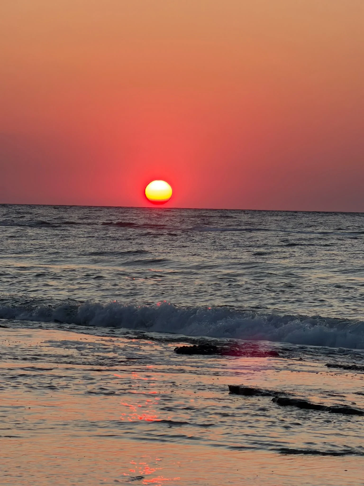 A sunset over the ocean with the sun near the horizon, casting pink, orange, and red hues across the sky and reflecting on the water surface.