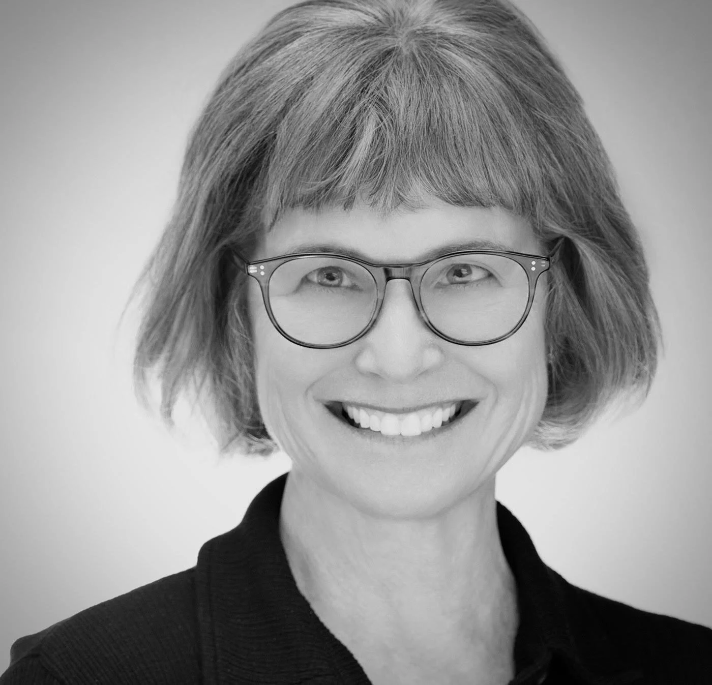 Black and white portrait of a smiling woman with short hair and glasses, wearing a dark blazer.