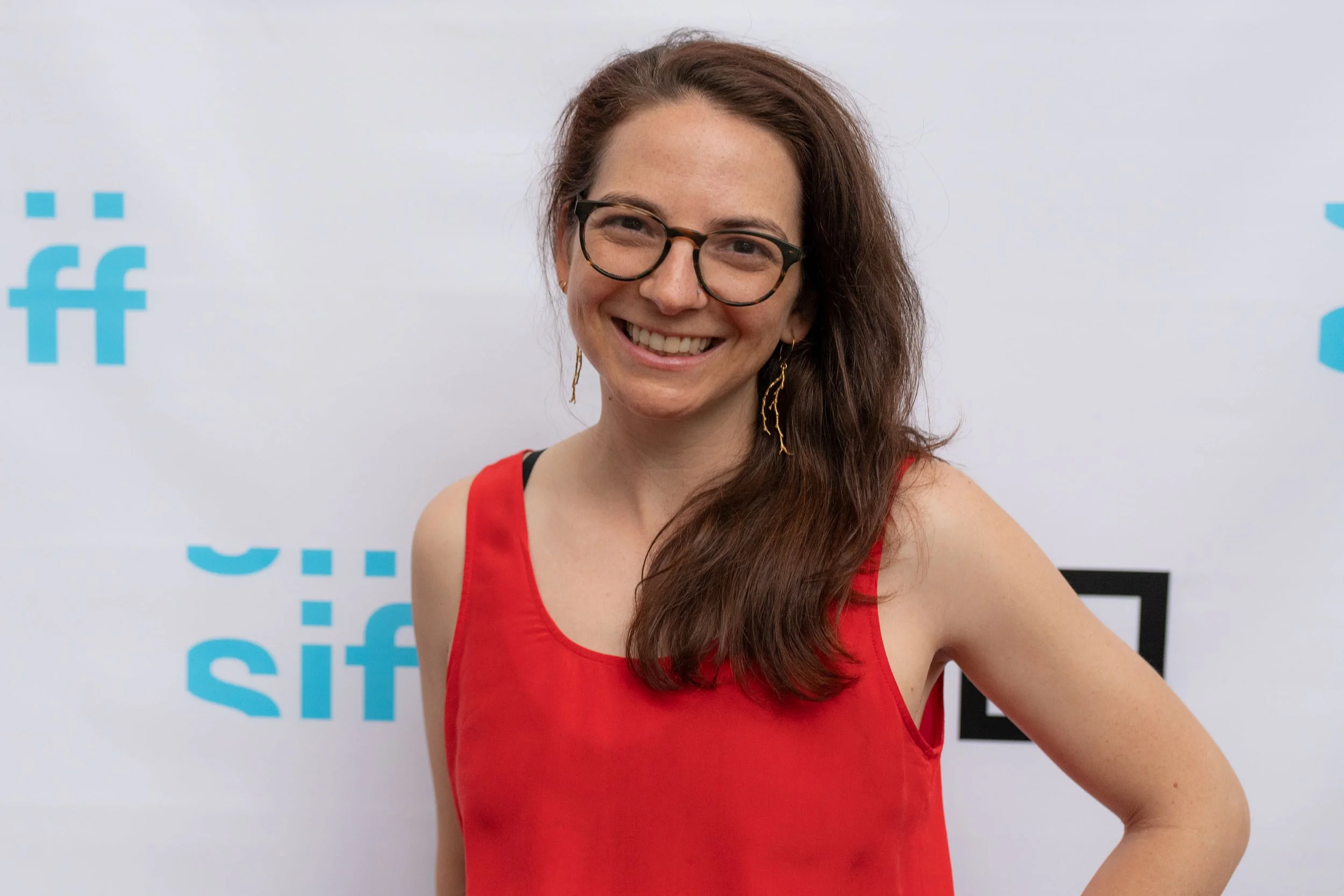 Smiling woman wearing glasses and a red sleeveless top in front of a branded backdrop