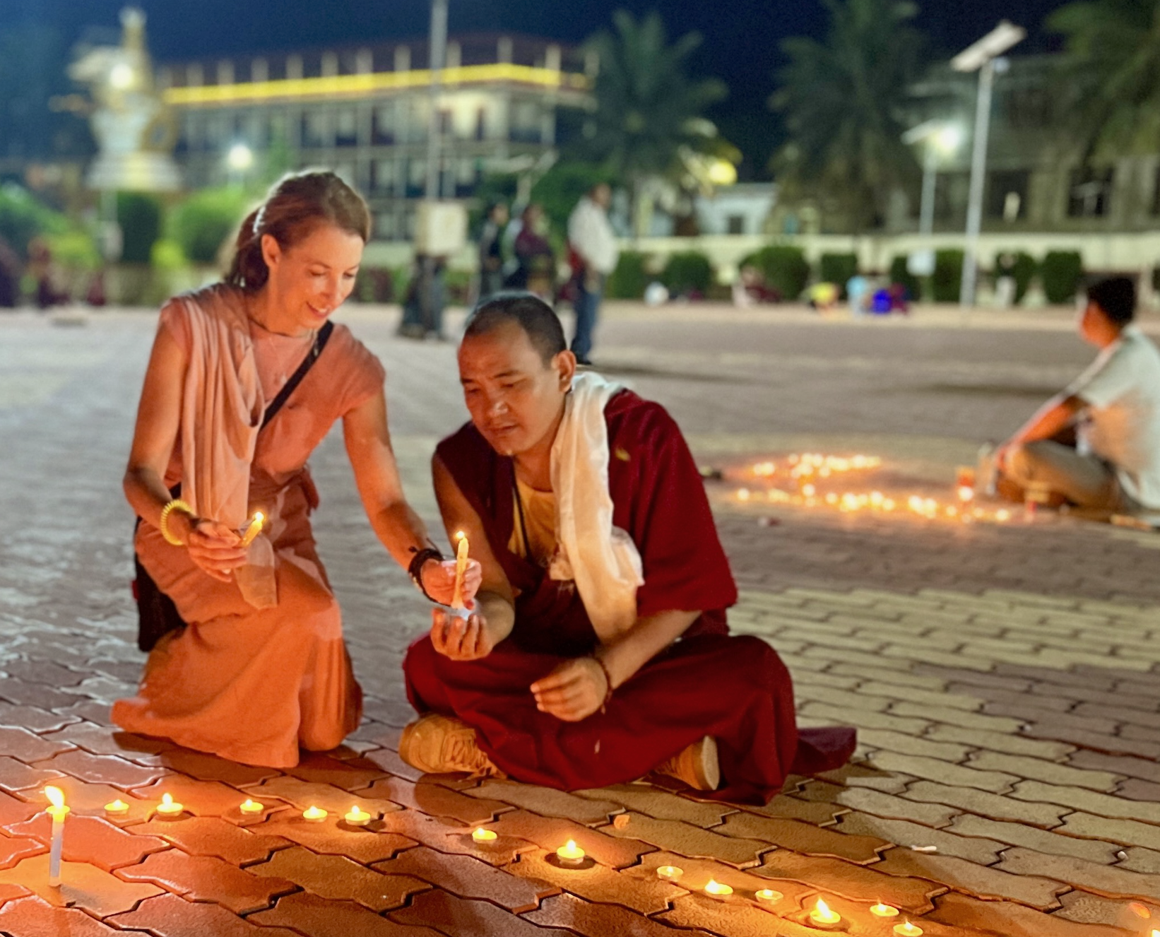 Woman and Buddhist monk lighting candles during a nighttime ceremony in a temple courtyard