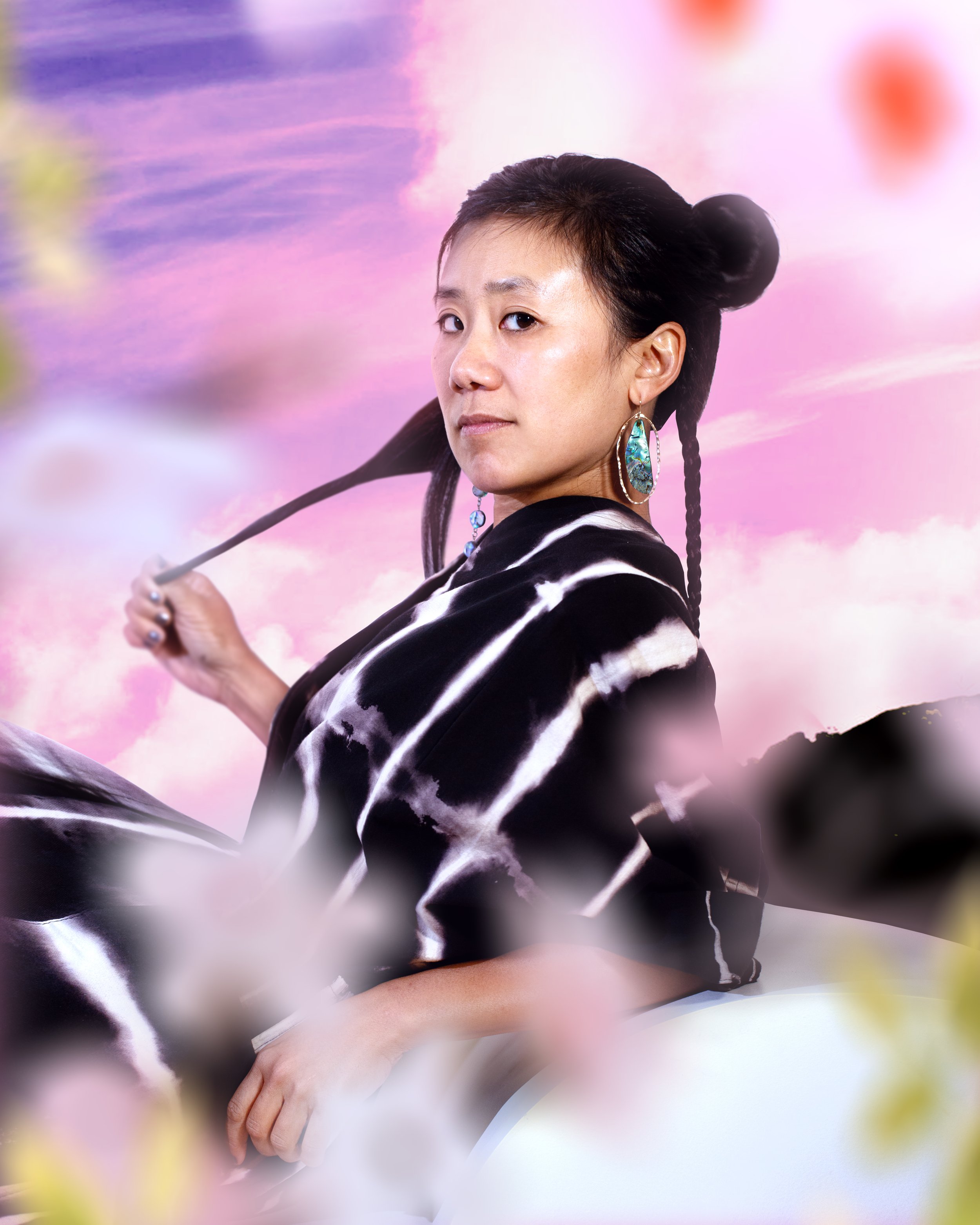 Woman with braided hair and turquoise earrings holding a paintbrush against a colorful pink and purple background