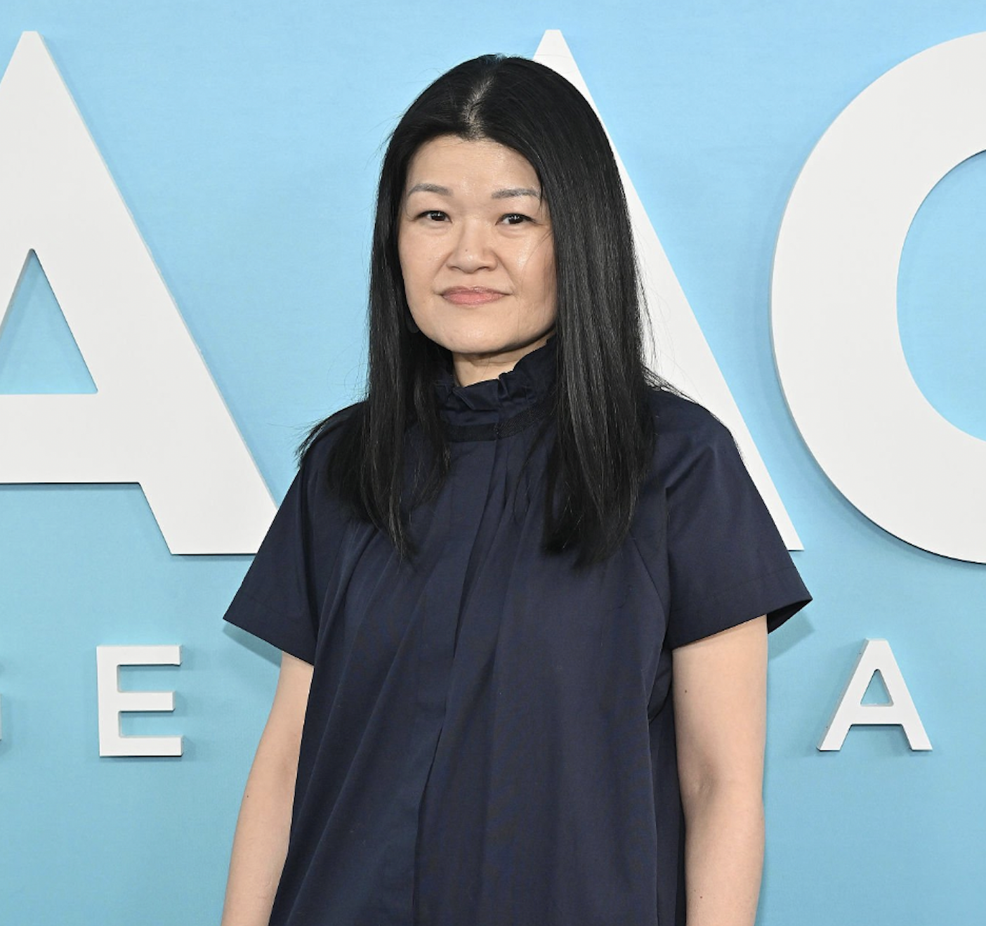 Portrait of an Asian woman with long black hair wearing a navy dress at a blue-background event