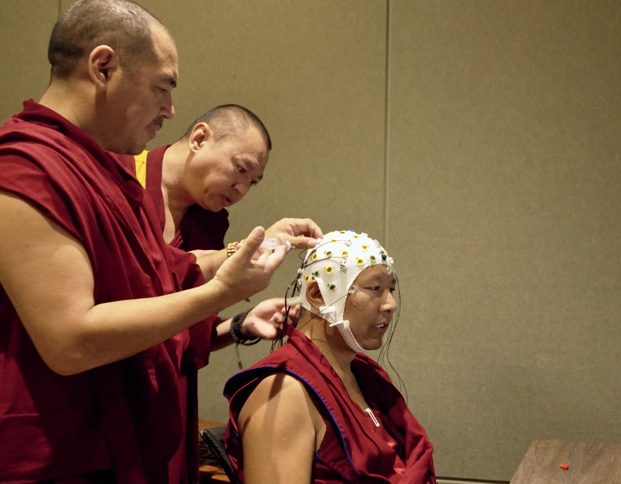 Monks attach electrodes to a seated person's EEG cap during a medical brainwave test.