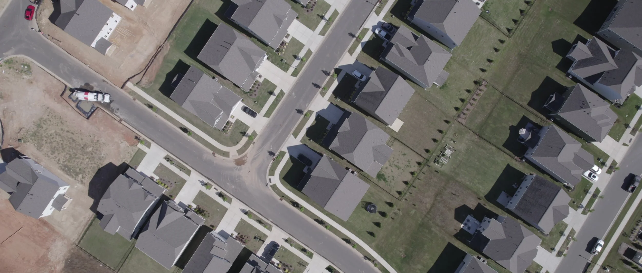 Aerial view of a residential neighborhood with houses, sidewalks, and parked cars along the streets.