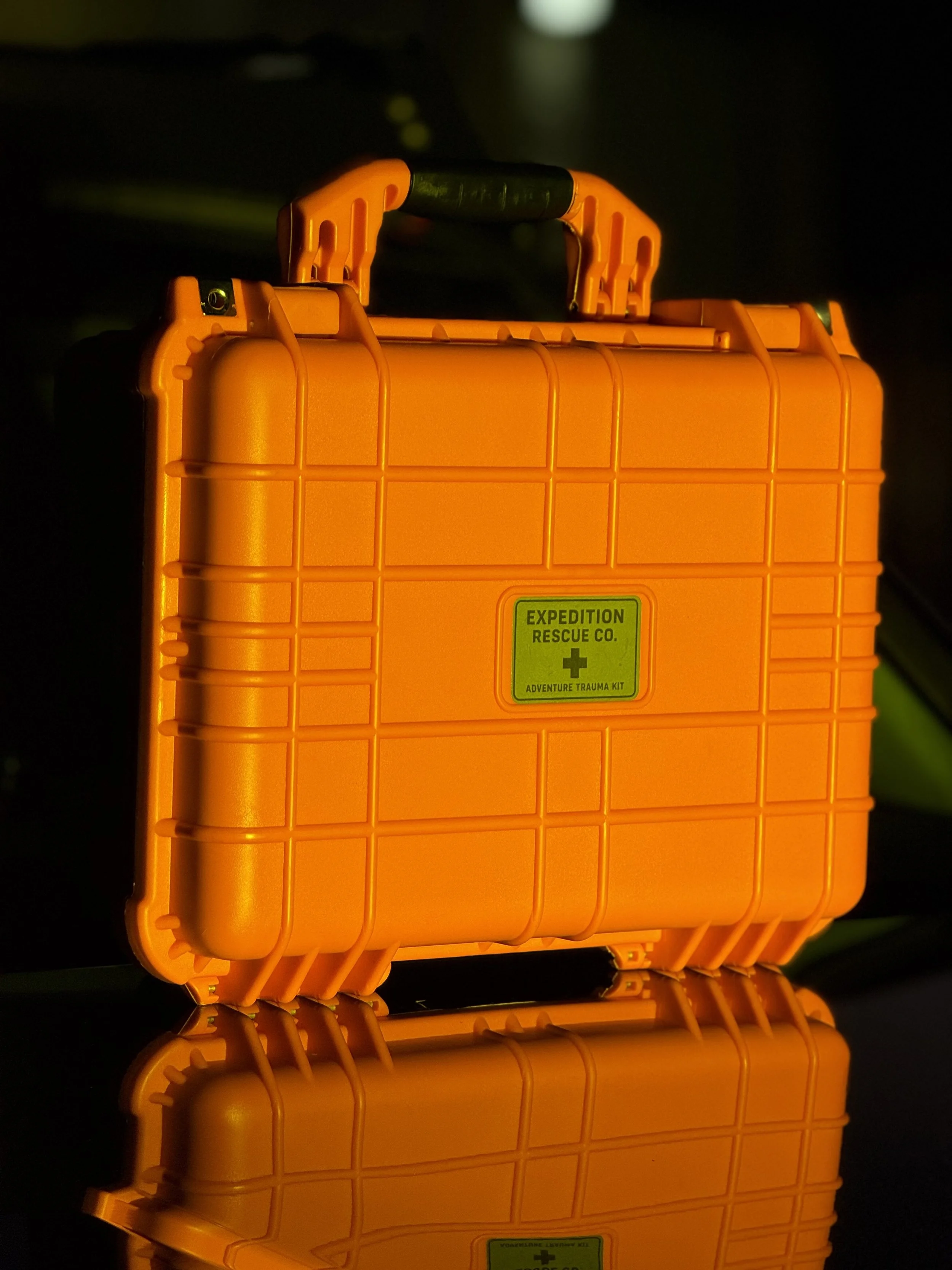 Orange plastic emergency trauma kit box labeled "Expedition Rescue Co. Adventure Trauma Kit" with a black handle, against a dark background.