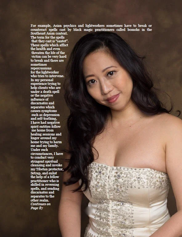 A woman with long black hair and a nose piercing, wearing a strapless beige embroidered top, standing against a brown background.