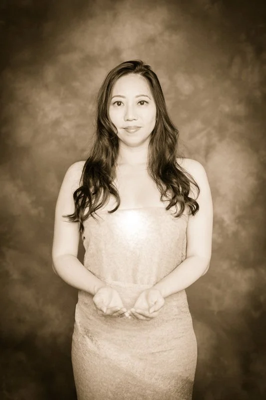 A woman with long wavy hair wearing a strapless dress standing in front of a textured background.