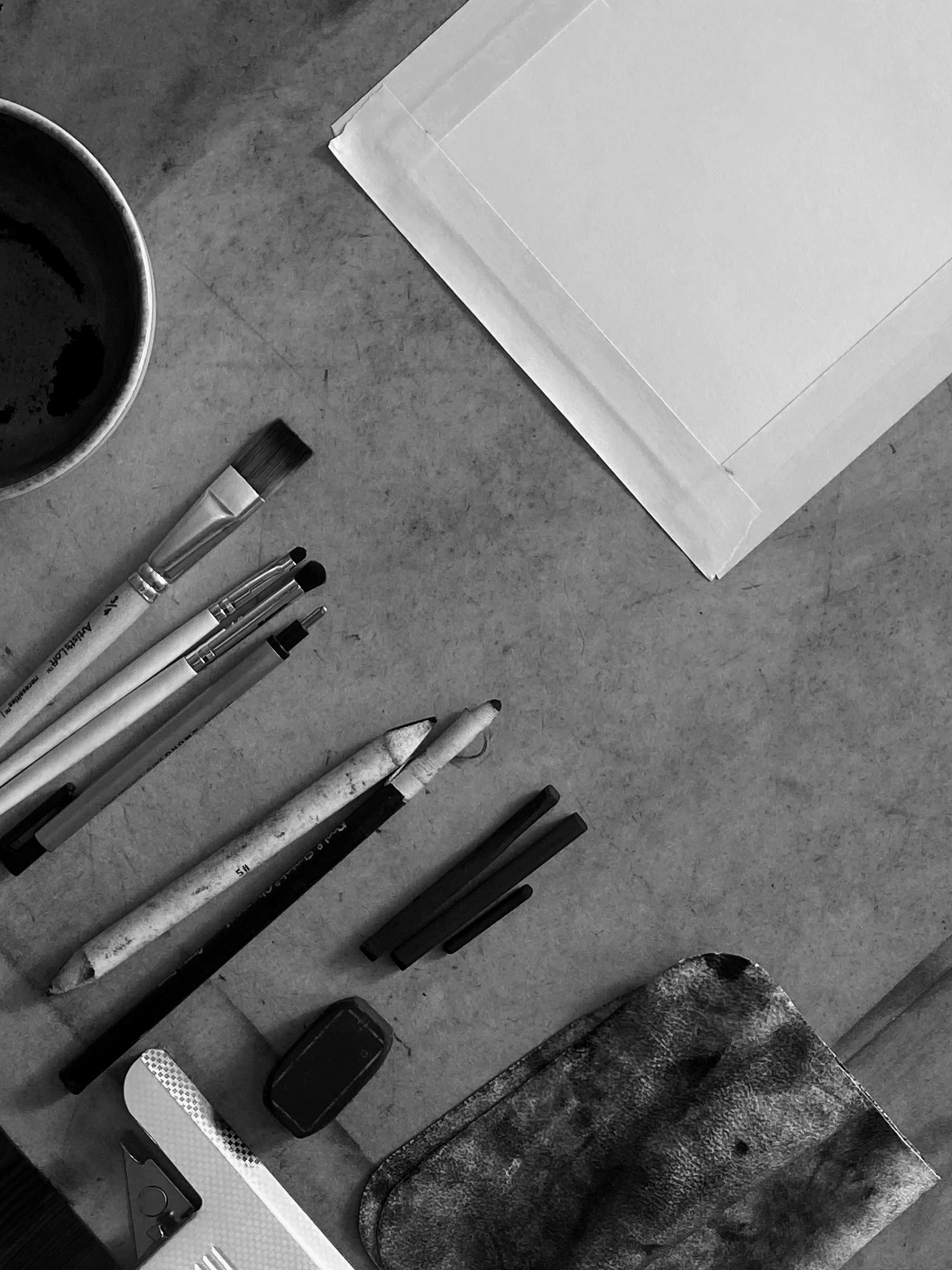A flat surface with various objects including strathmore charcoal paper, charcoal sticks, blending tools, tape - the whole artist set up.