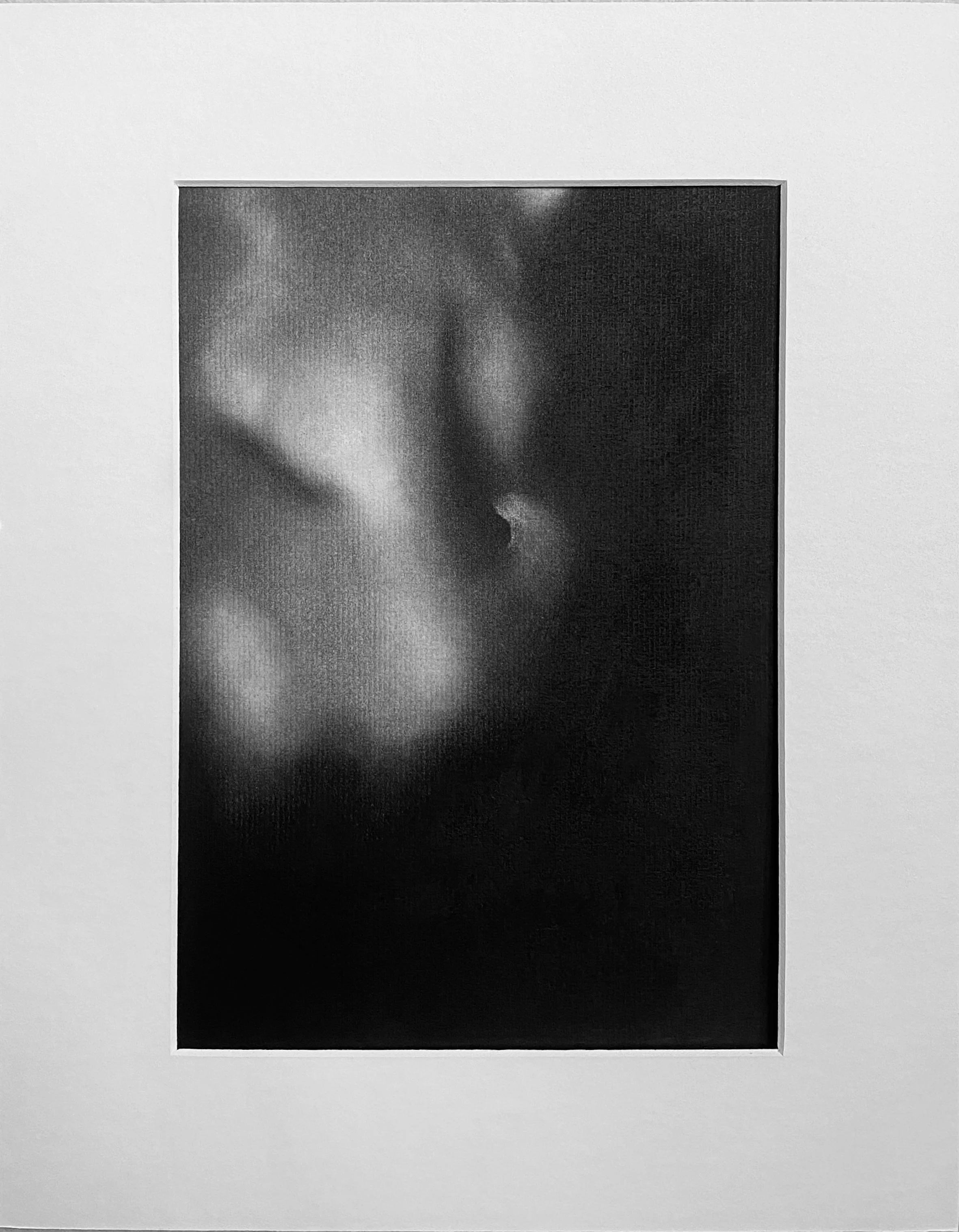 Black and white photographic print of a person's face, with emphasis on the eyes and nose, displayed within a white mat board on a gallery wall.