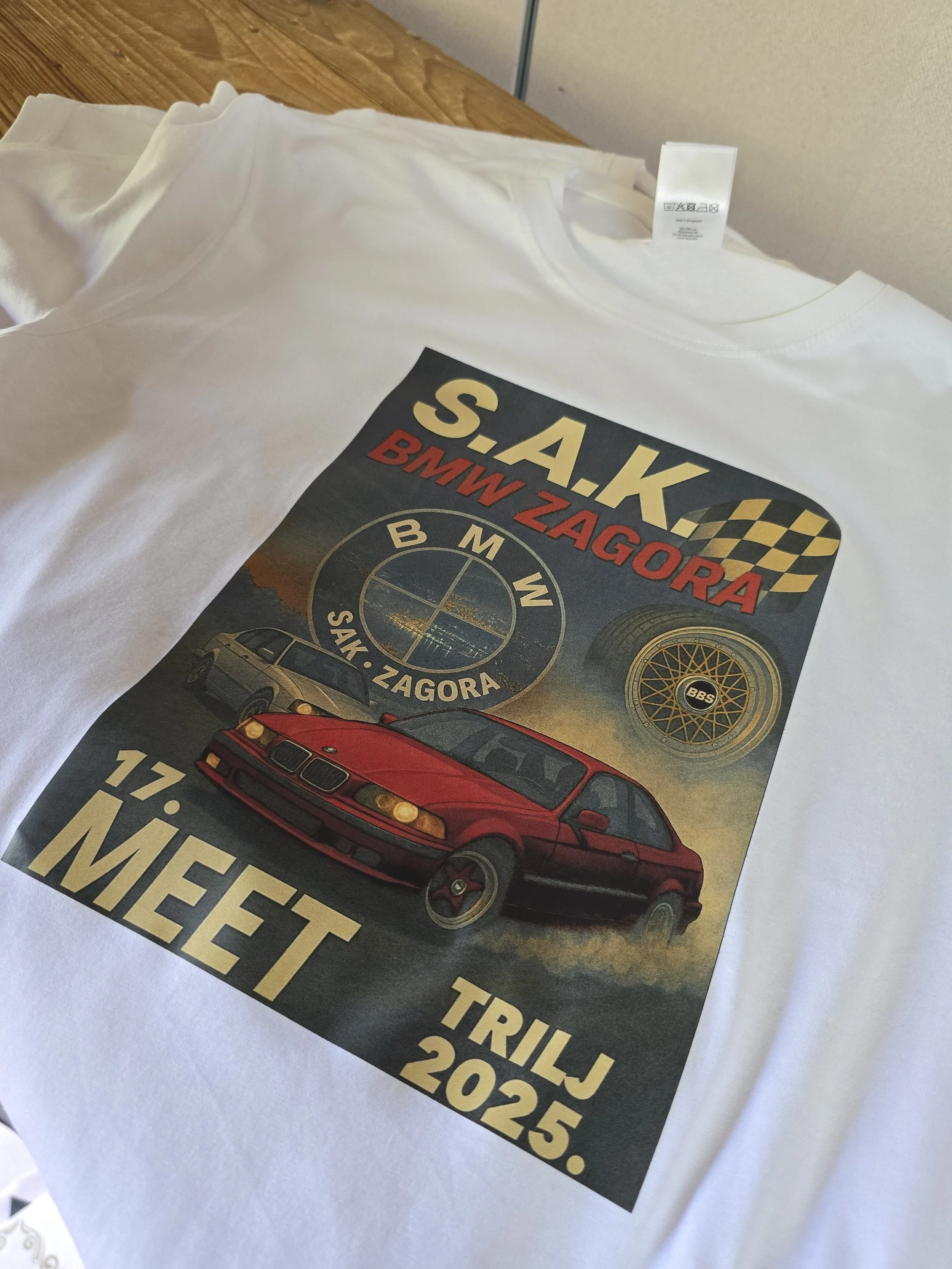 A white T-shirt with a graphic design and text about a BMW Z4 M Roadster car at a car event or triathlon in 2025, placed on top of a wooden surface.