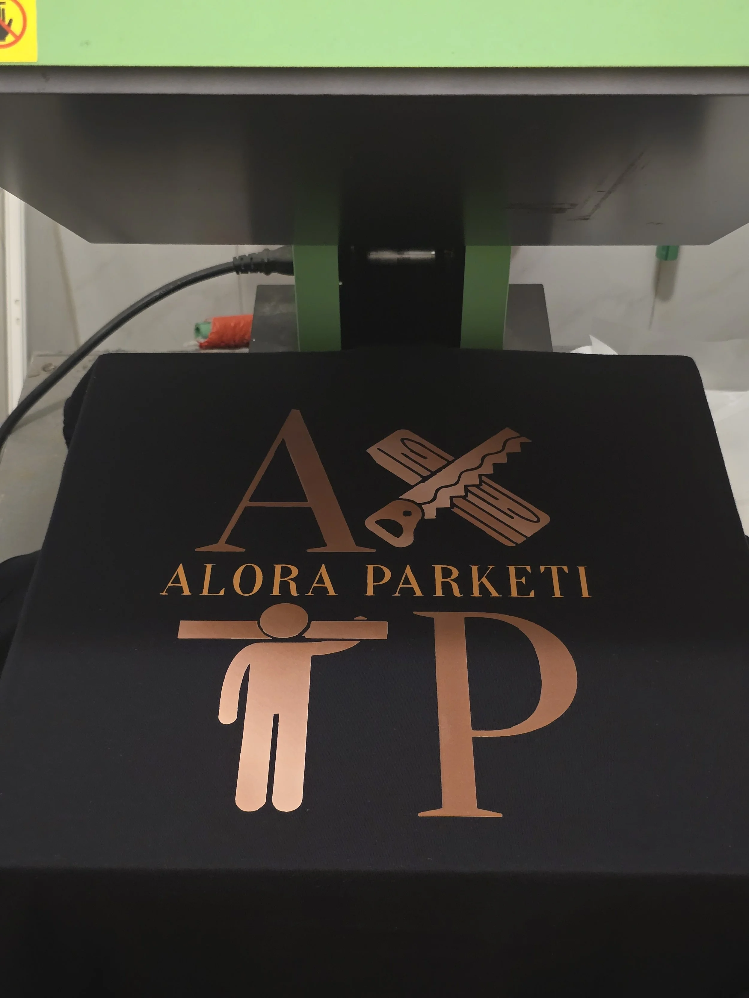 Close-up of a black packaging box with a pinkish logo and text that reads 'ALORA PARKETI' and a stylized figure of a person.