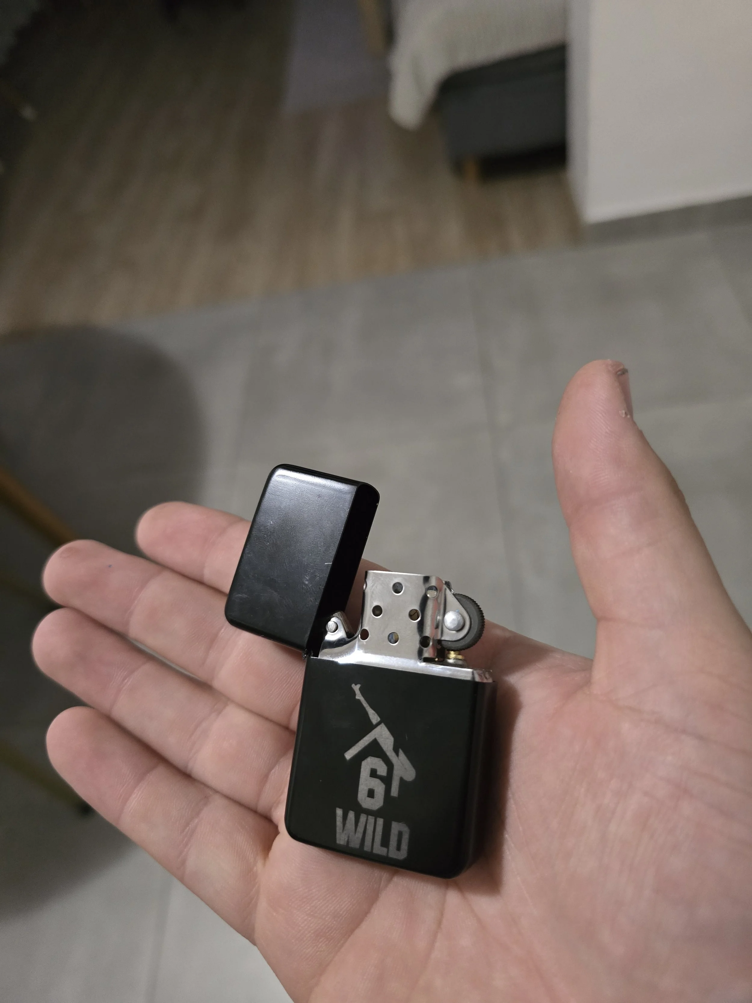 A hand holding a black disposable lighter with a metal top, with the words 'WILD RIDE' written on it.