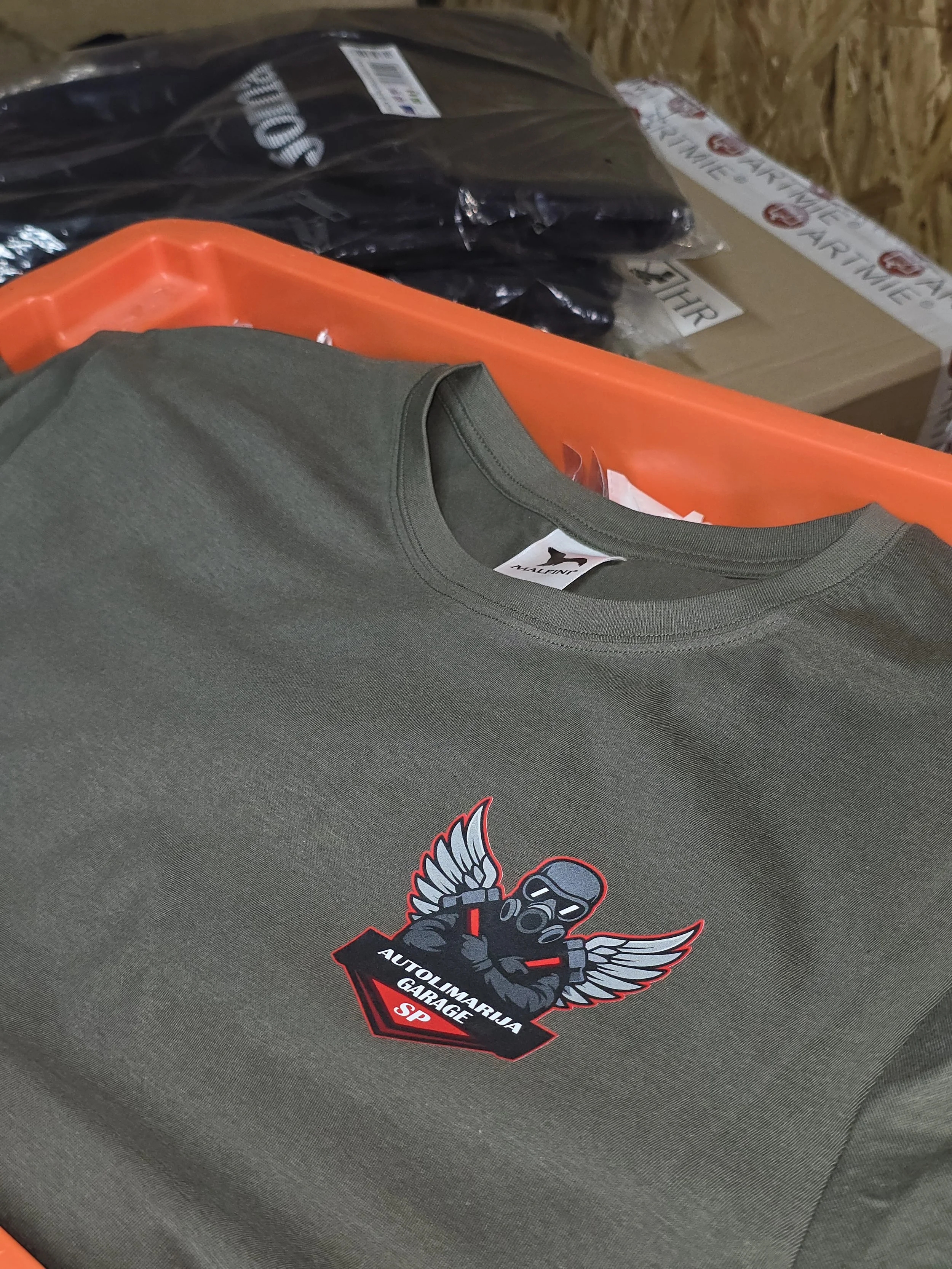 Close-up of a mounted sticker on a gray item, featuring a stylized bird with sunglasses and a spellbook, with text that reads 'Autoli Matarja Garage SP.'