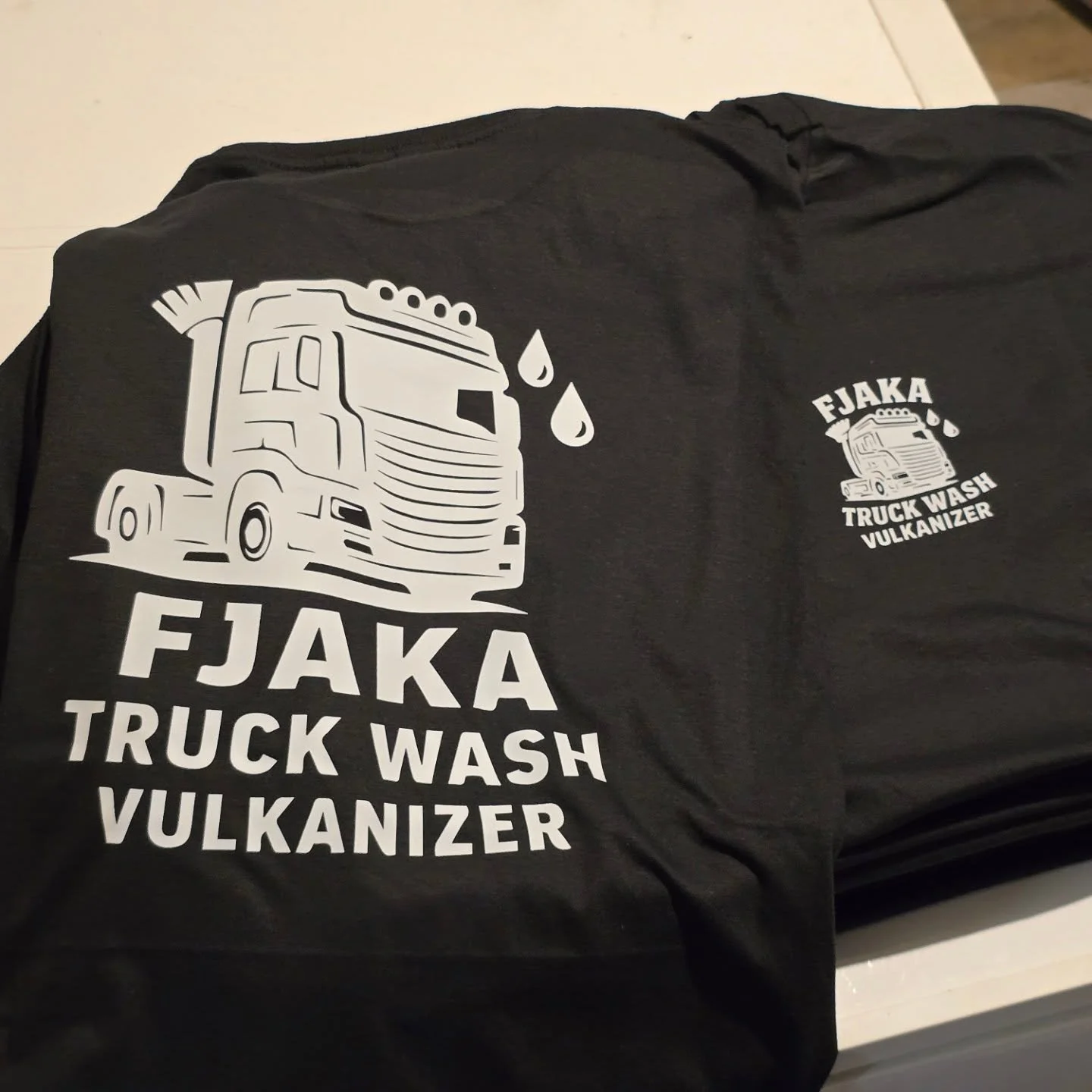 Black T-shirt with a white graphic of a truck with drops of water and the text "FJAKA TRUCK WASH VULKANIZER."