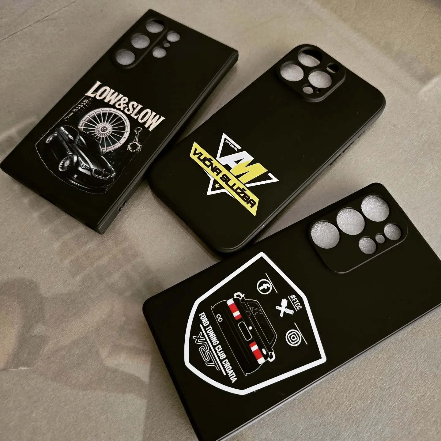 Three black smartphones with car-themed stickers and decals on a gray surface.
