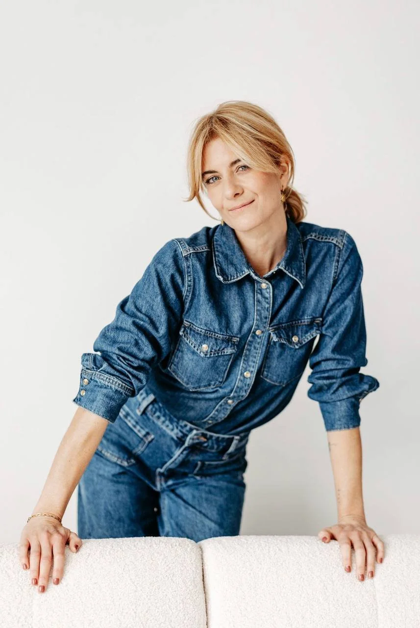 Eine Frau mit blonden Haaren trägt eine bluejeans und lehnt sich auf ein weißes Sofa.