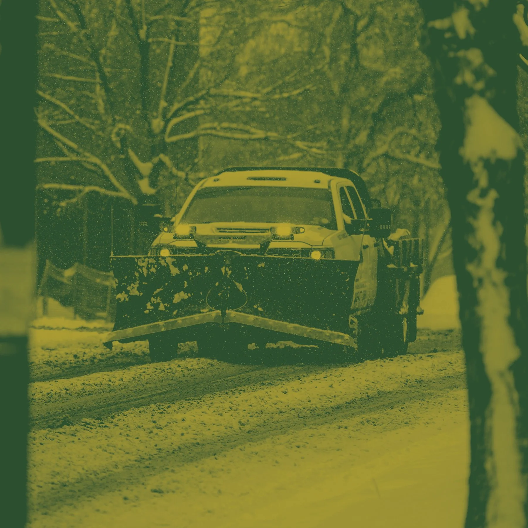 A police car on a snow-covered road at night, surrounded by leafless trees and a person standing beside the vehicle.