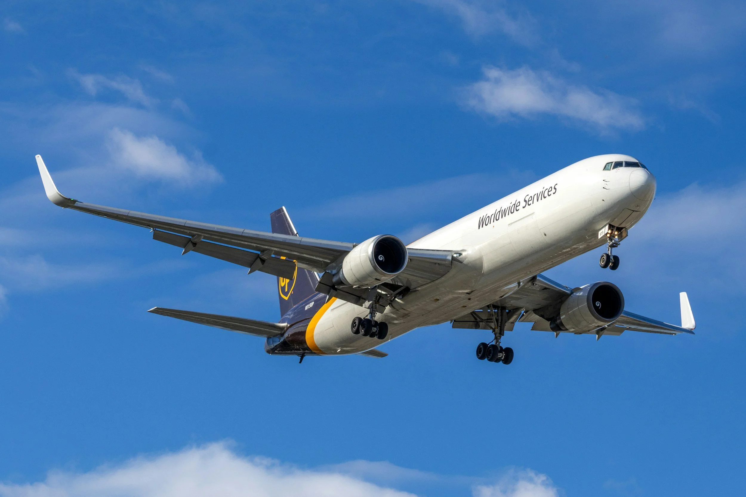 A white commercial airplane with the words 'Worldwide Services' on its side, flying through a blue sky with some clouds.