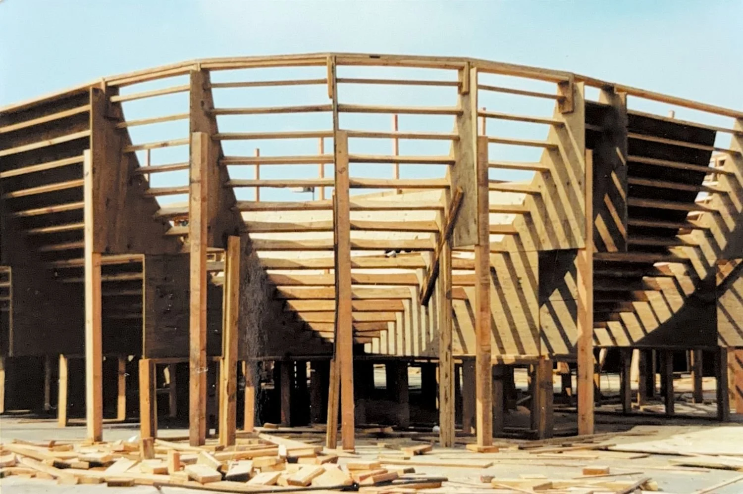 Wooden framing structure of a building under construction with scattered lumber on the ground.