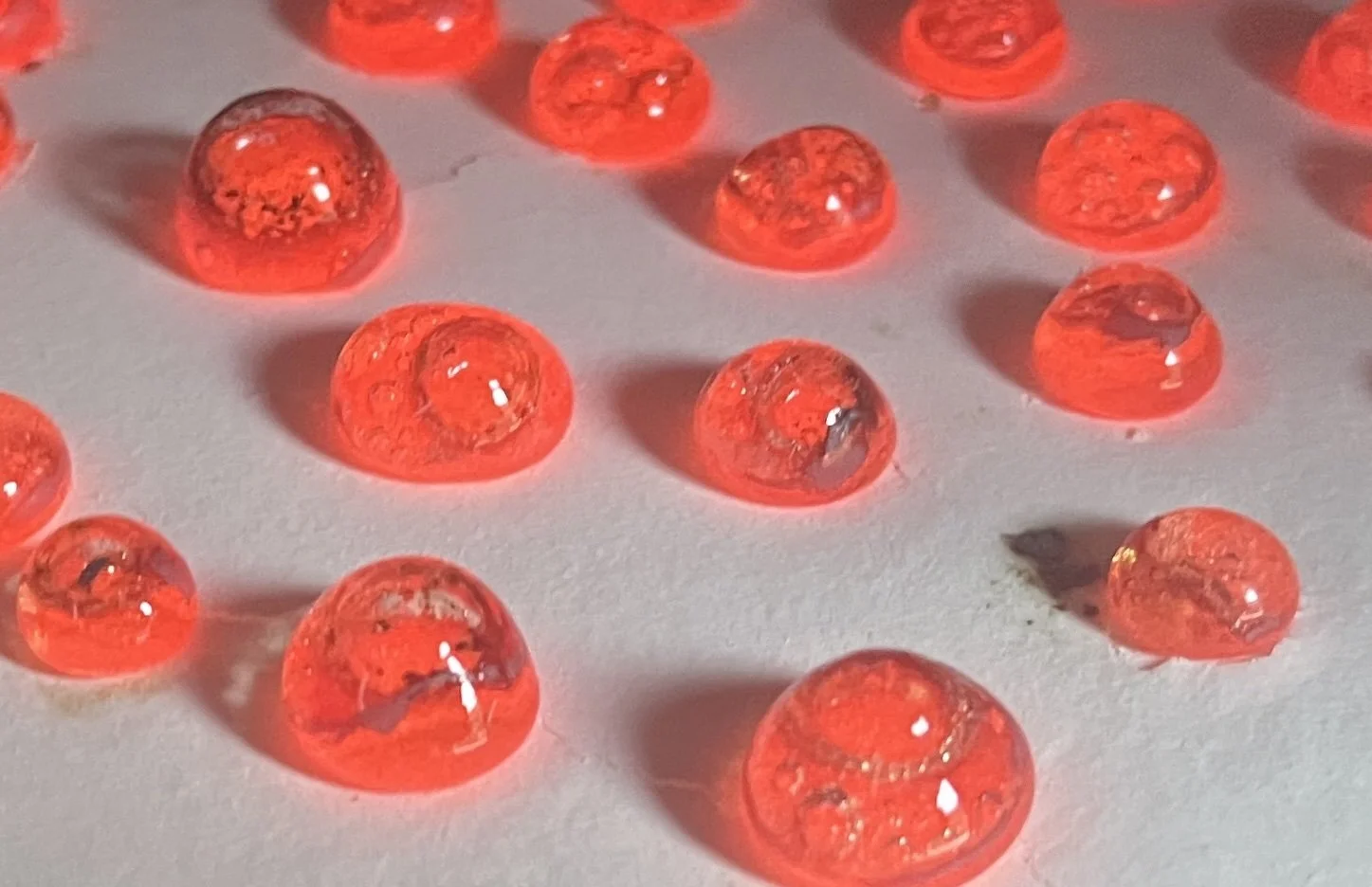 Gouttes de gelée rouge brillantes posées sur une surface blanche, créant des ombres allongées.