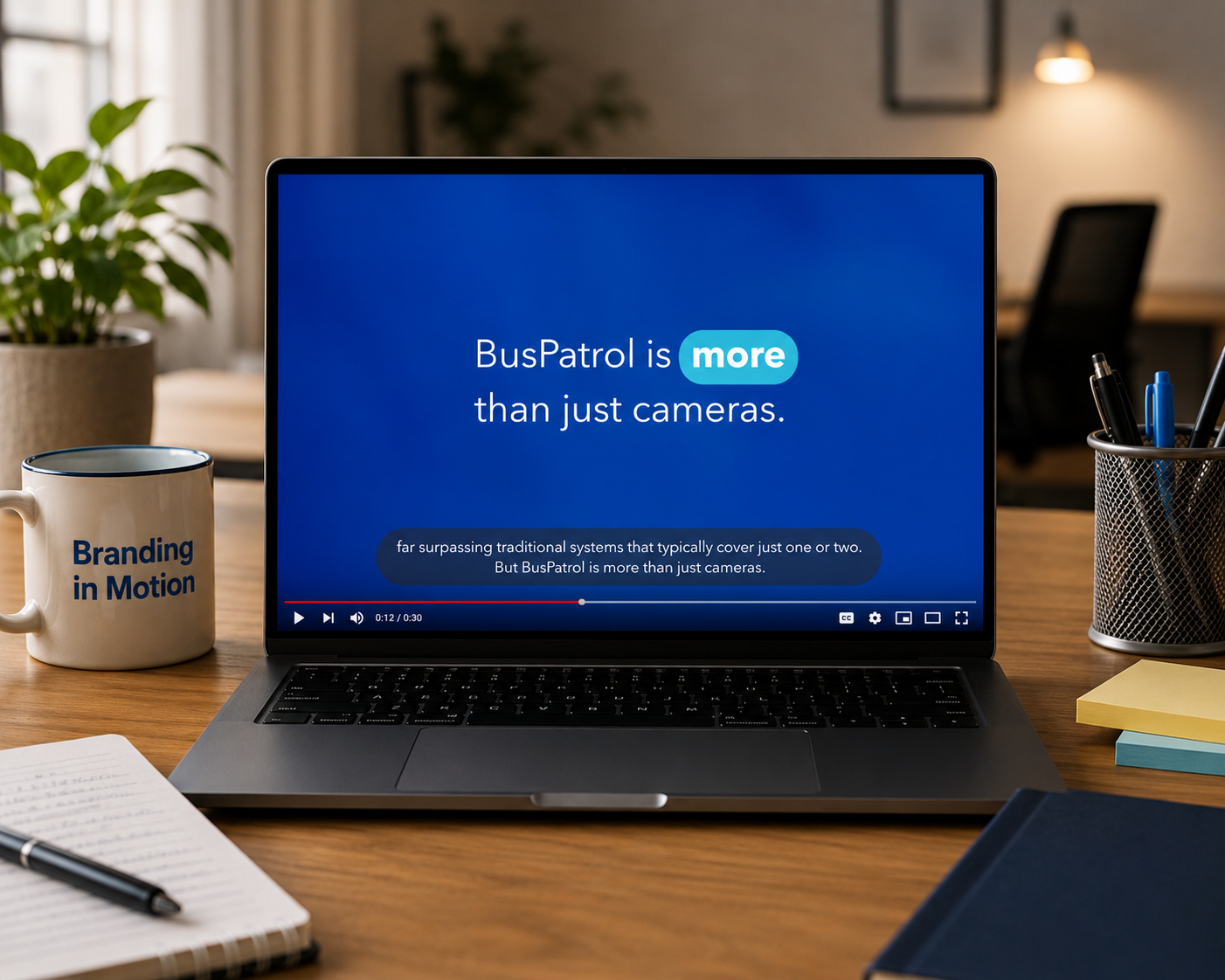 A laptop displaying a presentation slide on a wooden desk with a coffee mug, notebooks, pens, and a plant in the background.