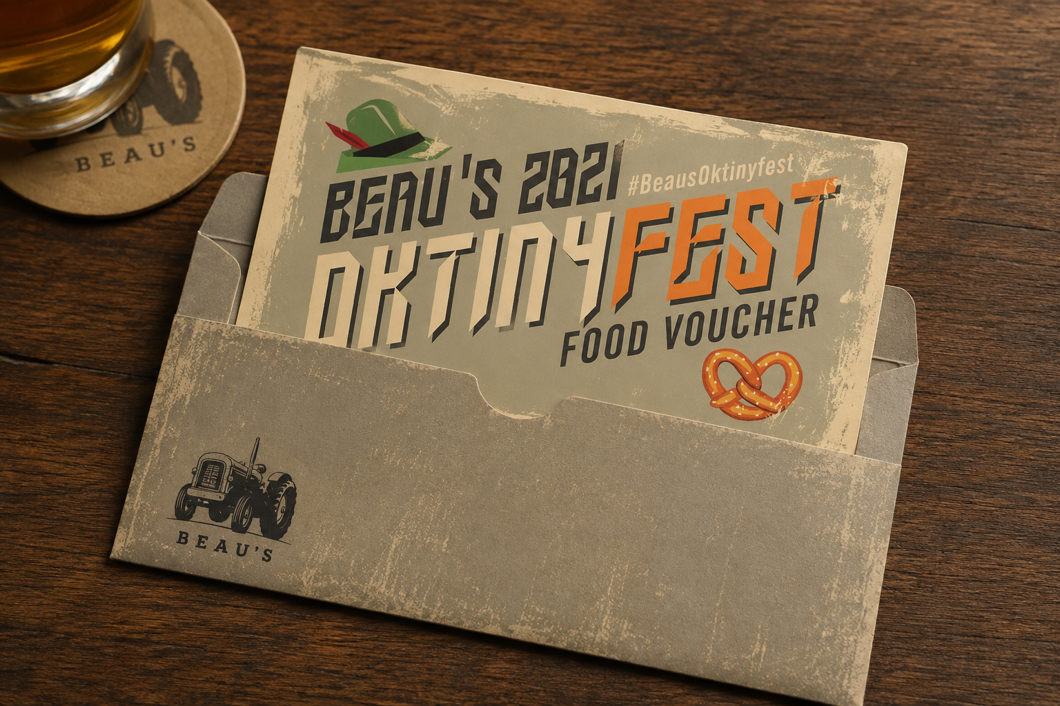 Food voucher inside a gray envelope with a tractor illustration, placed on a wooden table with a beer glass on a coaster nearby.