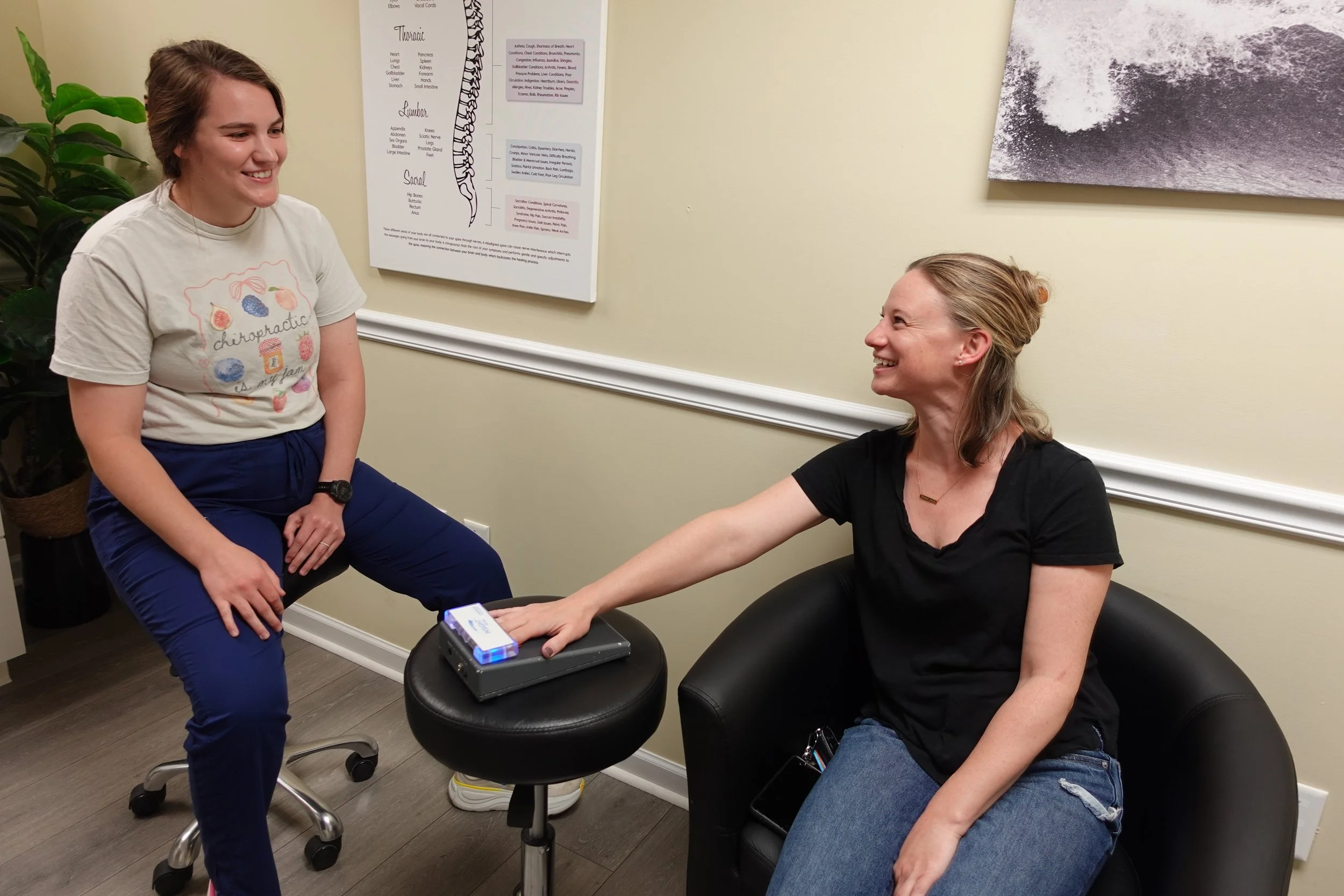 A woman receiving CLA INSiGHT Scans  from a chiropractor assistant, with both women smiling in a clinical setting.