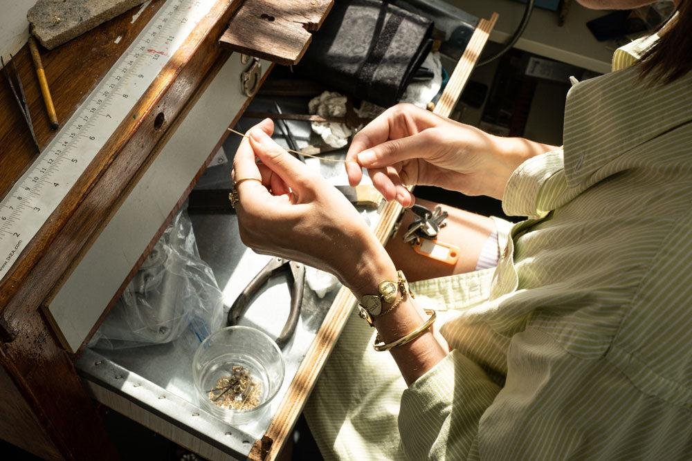 A person working at a jewelry bench, assembling or repairing jewelry with small tools and materials.