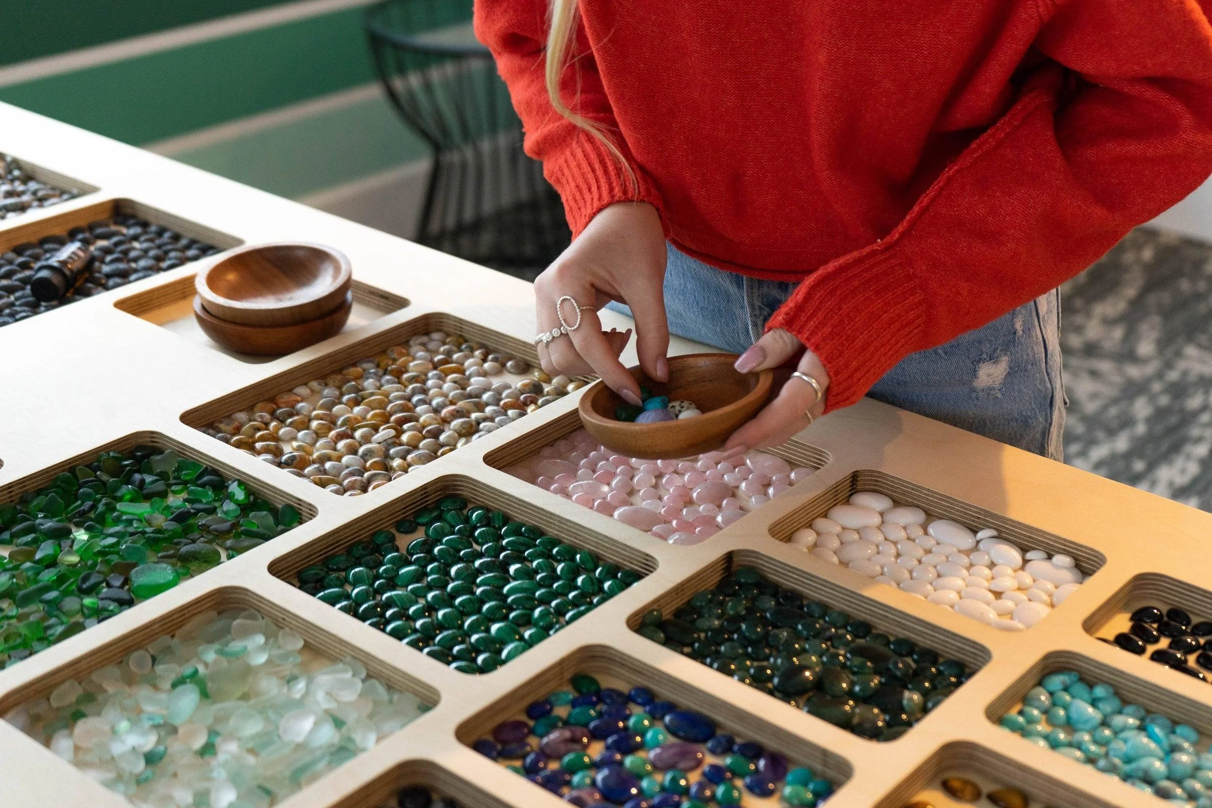 Person selecting marbles from a wooden box with multiple compartments of colorful marbles.