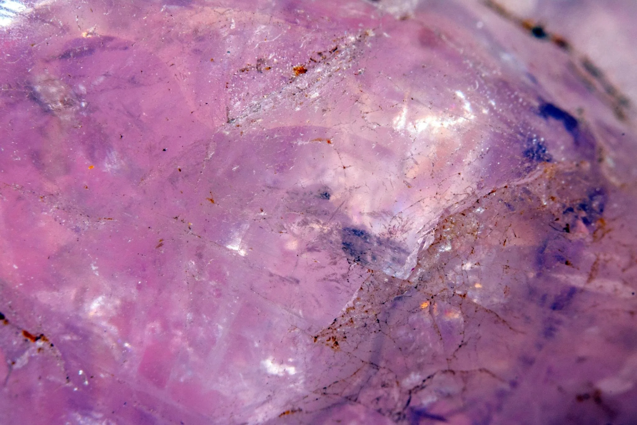 Close-up of a pink mineral or gemstone surface with small black and brown specks and shiny areas.
