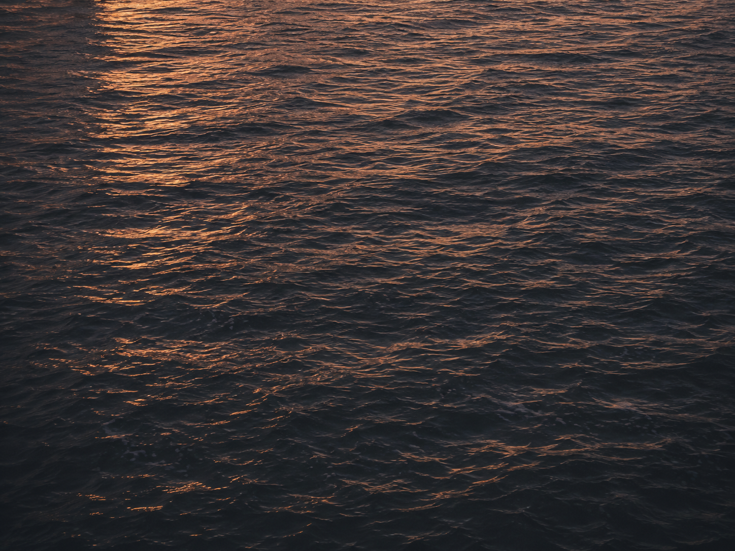 Meeresoberfläche bei Sonnenuntergang mit reflektierendem Licht auf den Wellen.