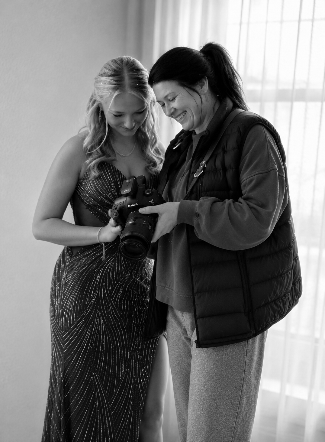 Two women, one holding a Canon camera, sharing a moment and smiling.