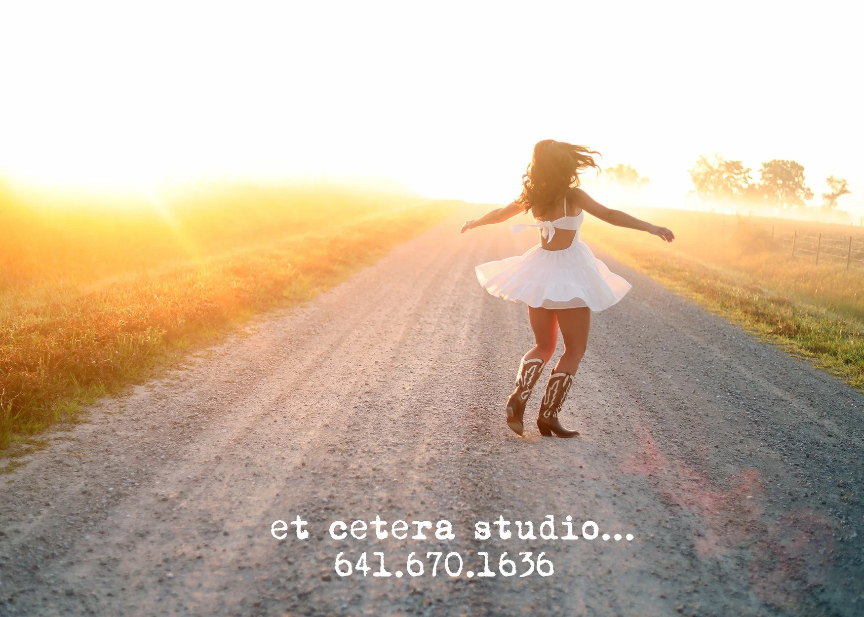 A woman in a white dress and cowboy boots is jumping and spinning on a gravel road at sunset or sunrise, with open fields and trees in the background, and contact information written at the bottom.