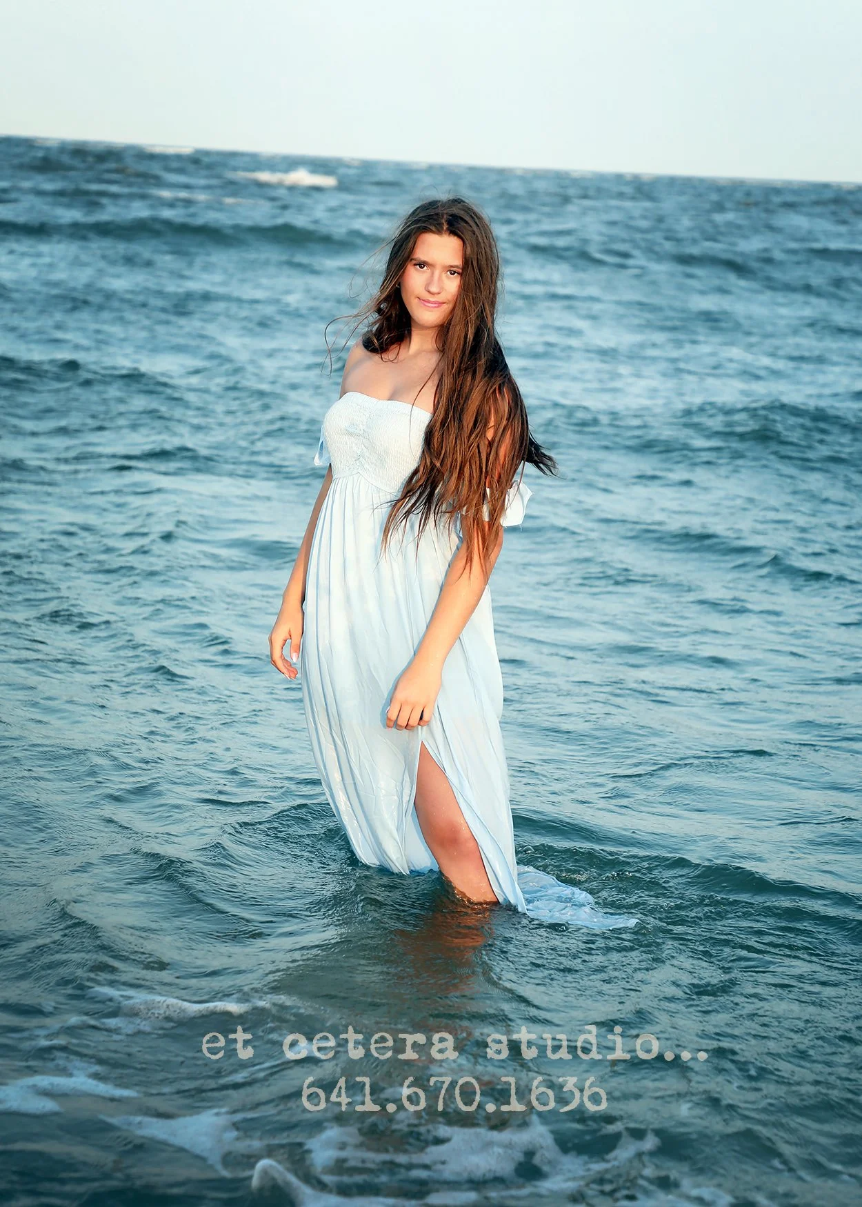 A woman in a white dress standing in the ocean, with text overlay promoting a studio and contact number.