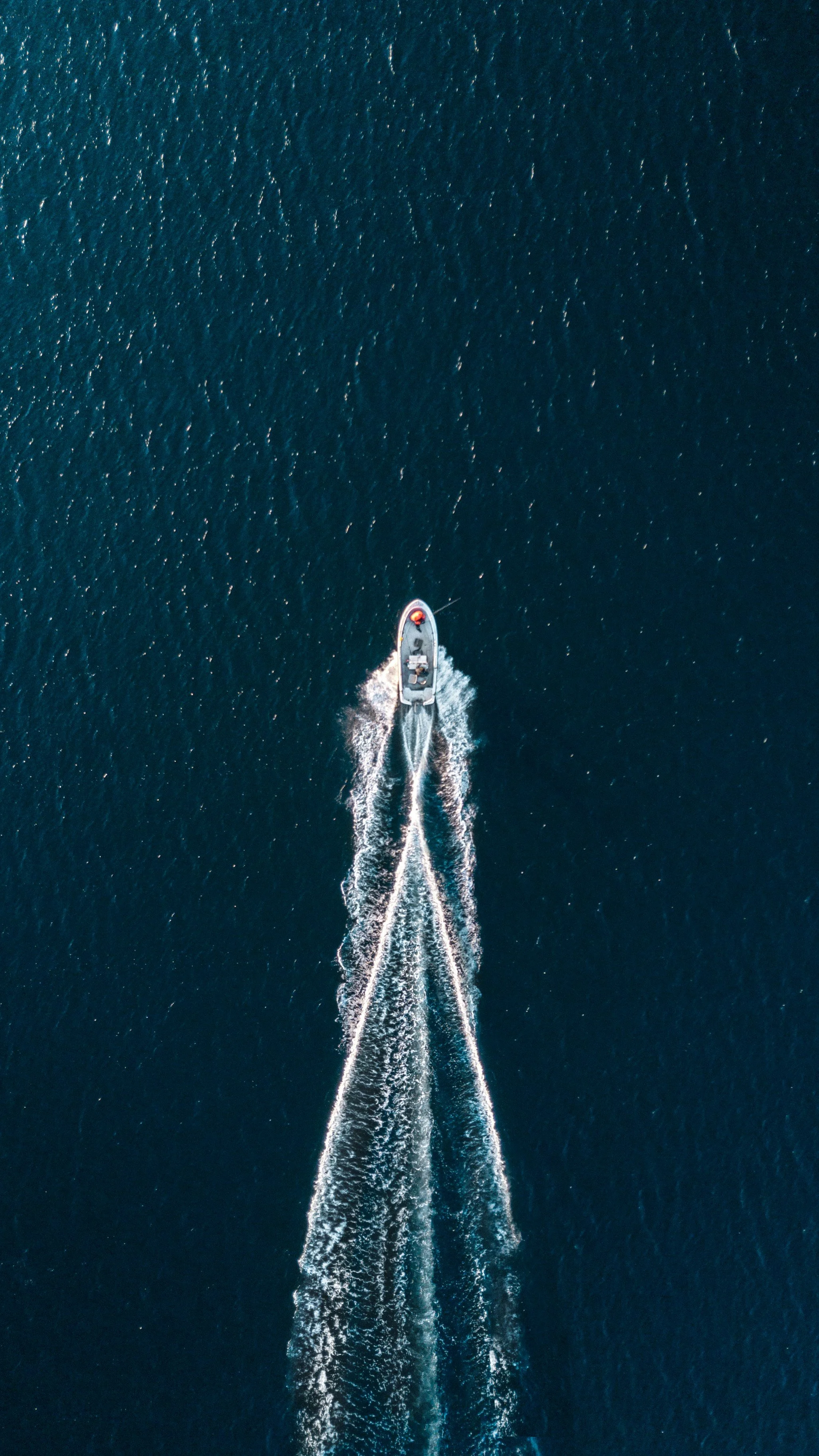 An aerial view of a small motorboat moving across dark blue water, creating a wake behind it.