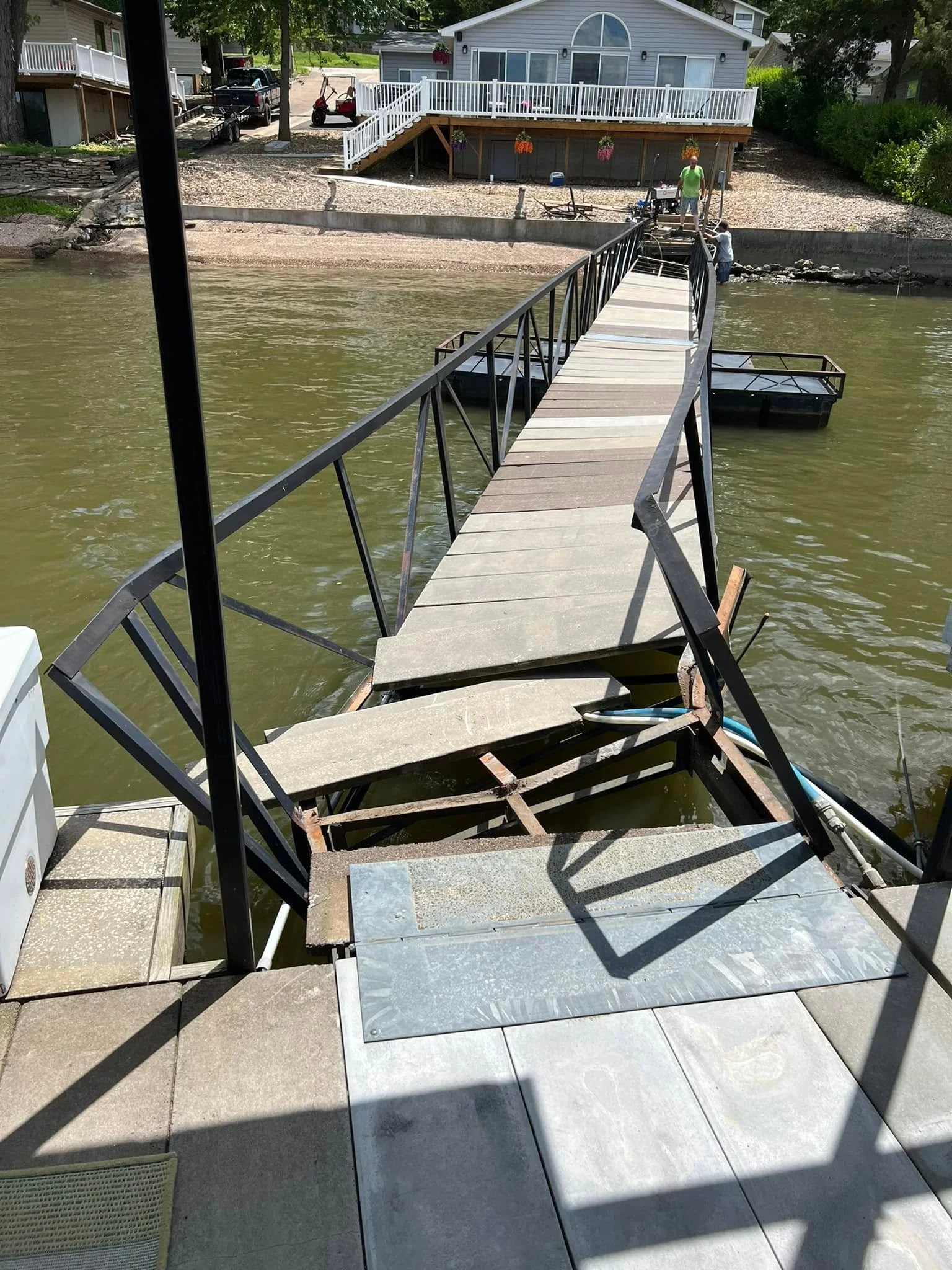 A dock under construction extends from a patio into a body of water. Two people are working on the dock, with tools and materials visible.