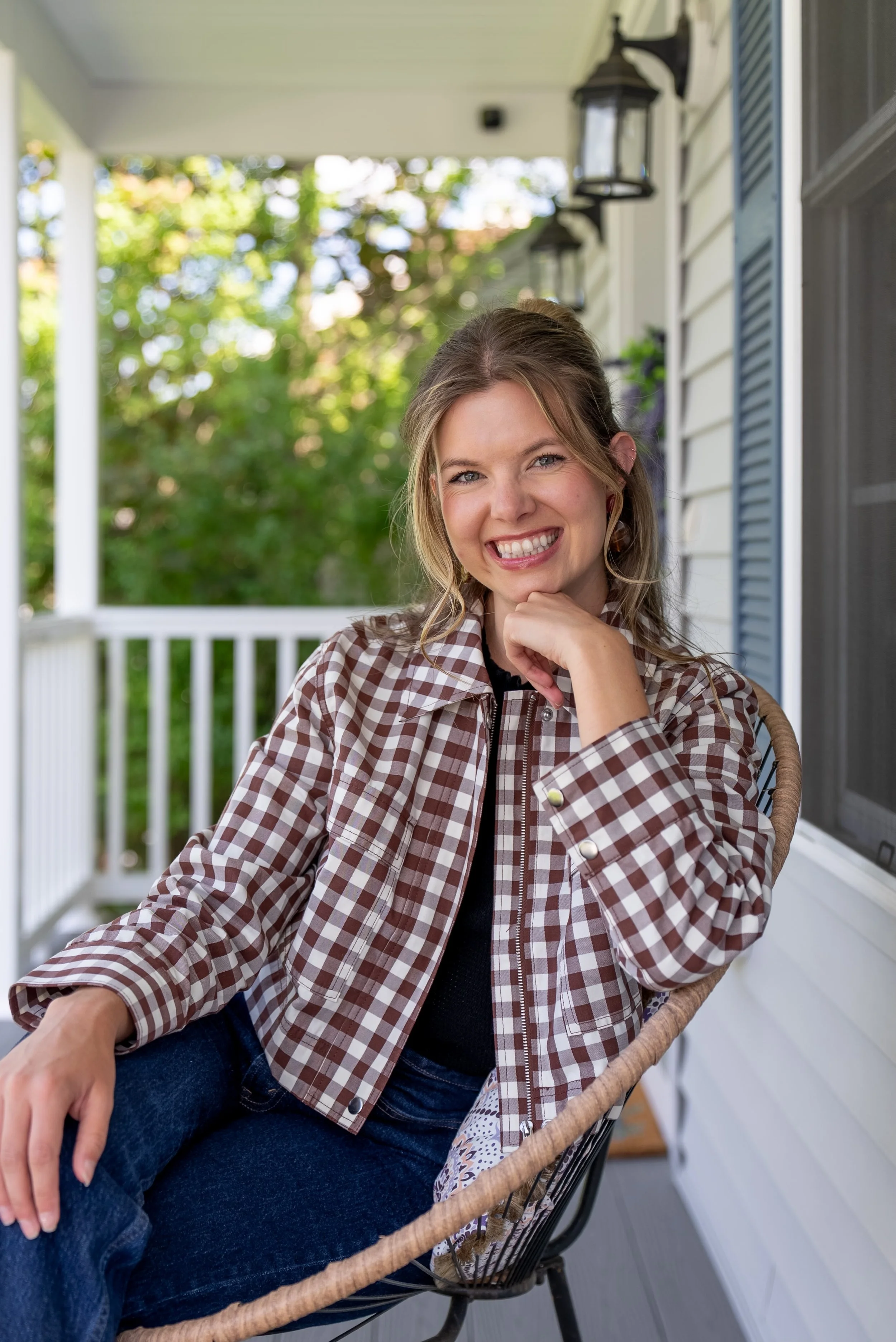 The owner of By Arlyss, Interior Styling, Arlyss sitting on the porch of a beautiful home. She is preparing for a styling consult for in person design.