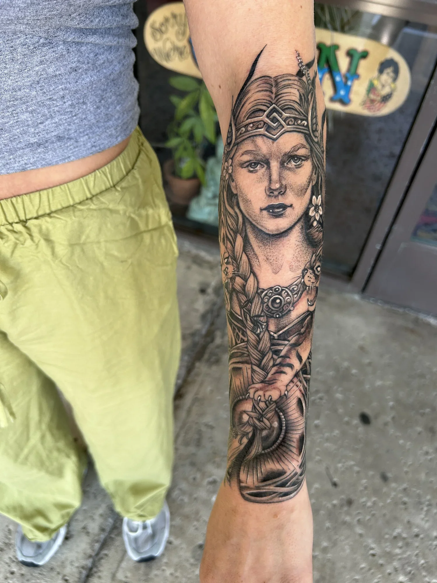 Detailed black and gray tattoo of a woman with long hair, wearing a crown, on the person's forearm.