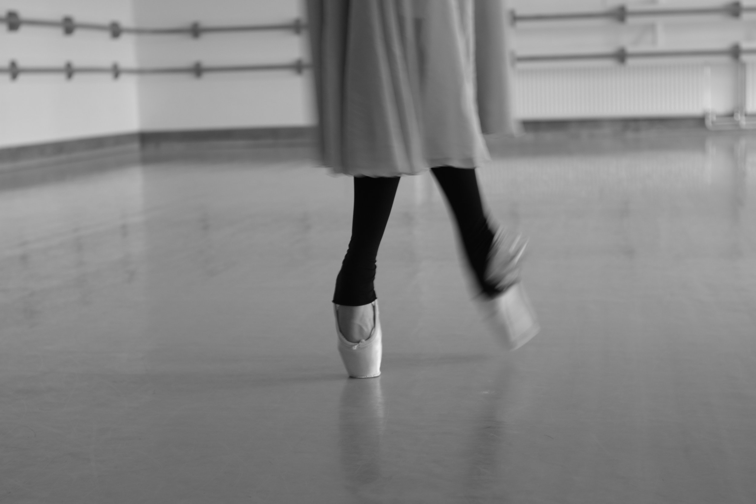 Close-up of a ballet dancer's legs and feet in pointe shoes on a dance studio floor.