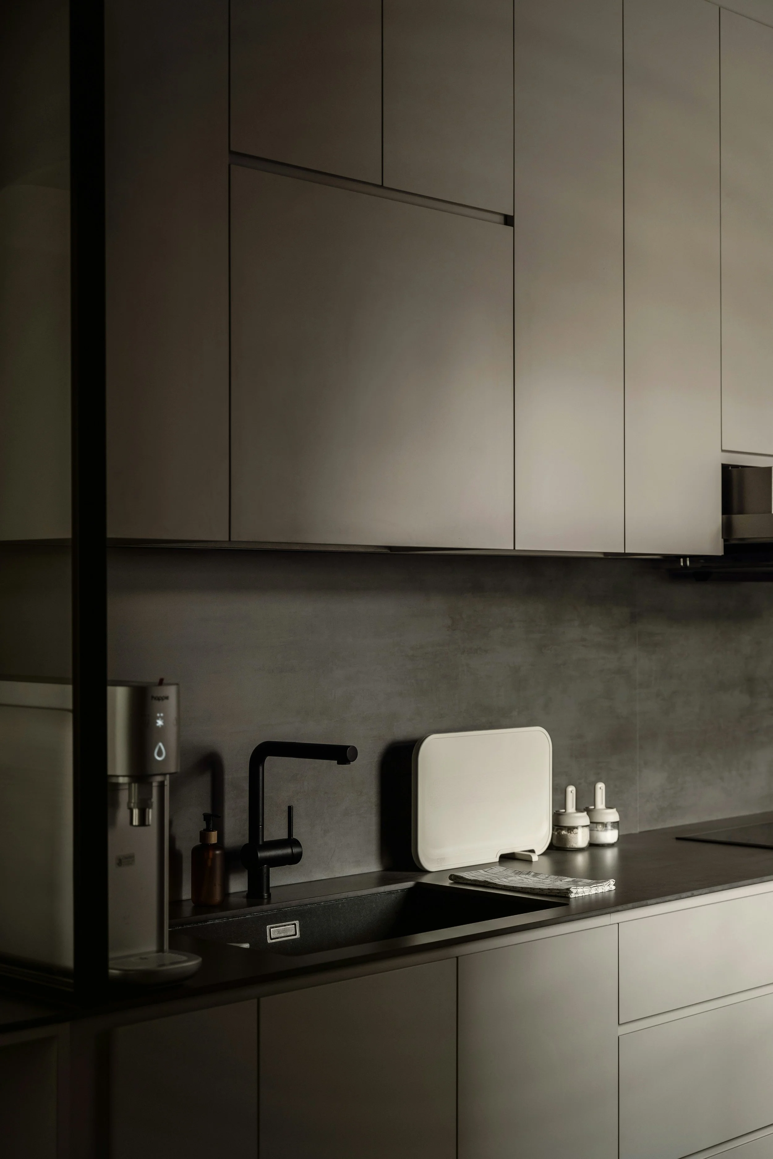Modern kitchen with upper and lower cabinets, a black faucet, a white drying rack, soap dispensers, a napkin, and a black countertop. No visible people or animals.