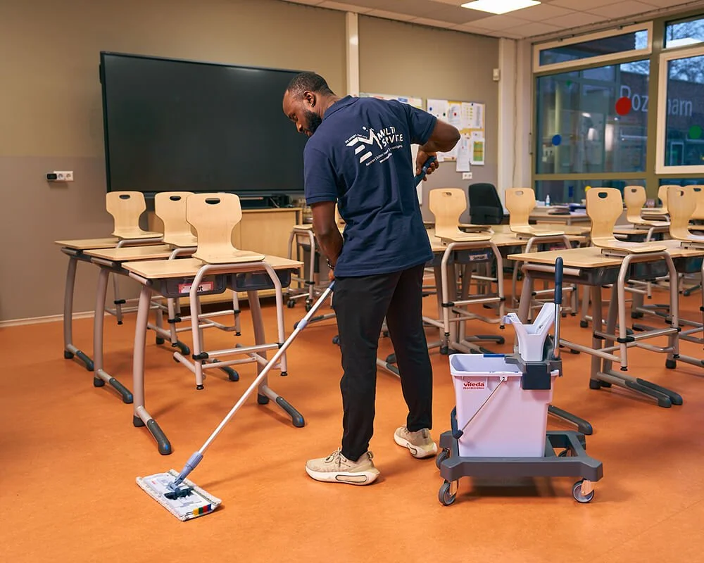 Man die een schoollokaal schoonmaakt met een mop en een mopwagen.