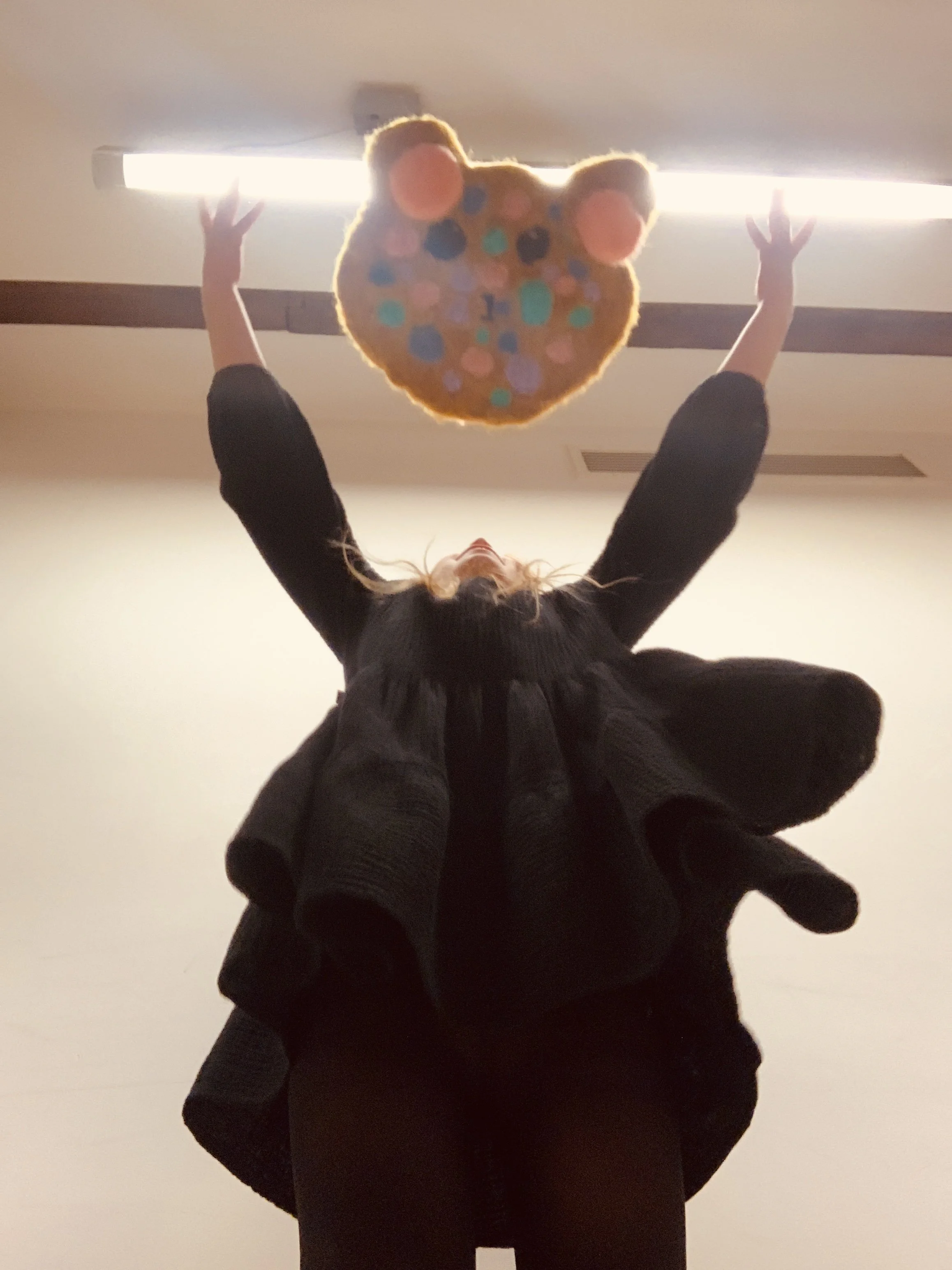 Person holding a colorful heart-shaped object with pudding-like decorations, reaching towards a ceiling light fixture.