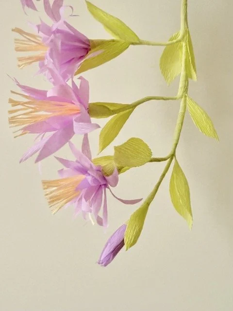 A paper craft of pink flowers with green leaves on a light background.