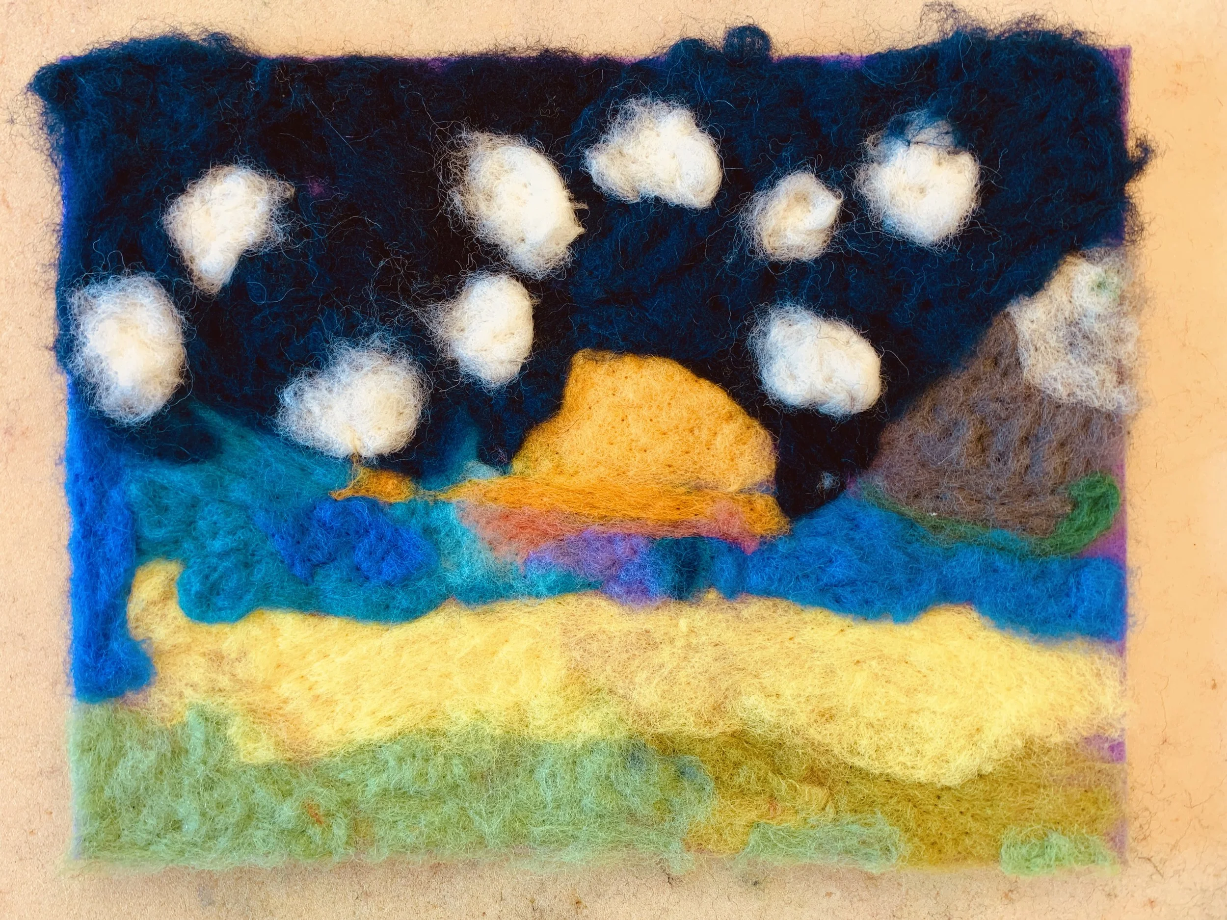 Felted art piece depicting a rainbow with clouds. The rainbow has vibrant colors, and the clouds are white and fluffy.