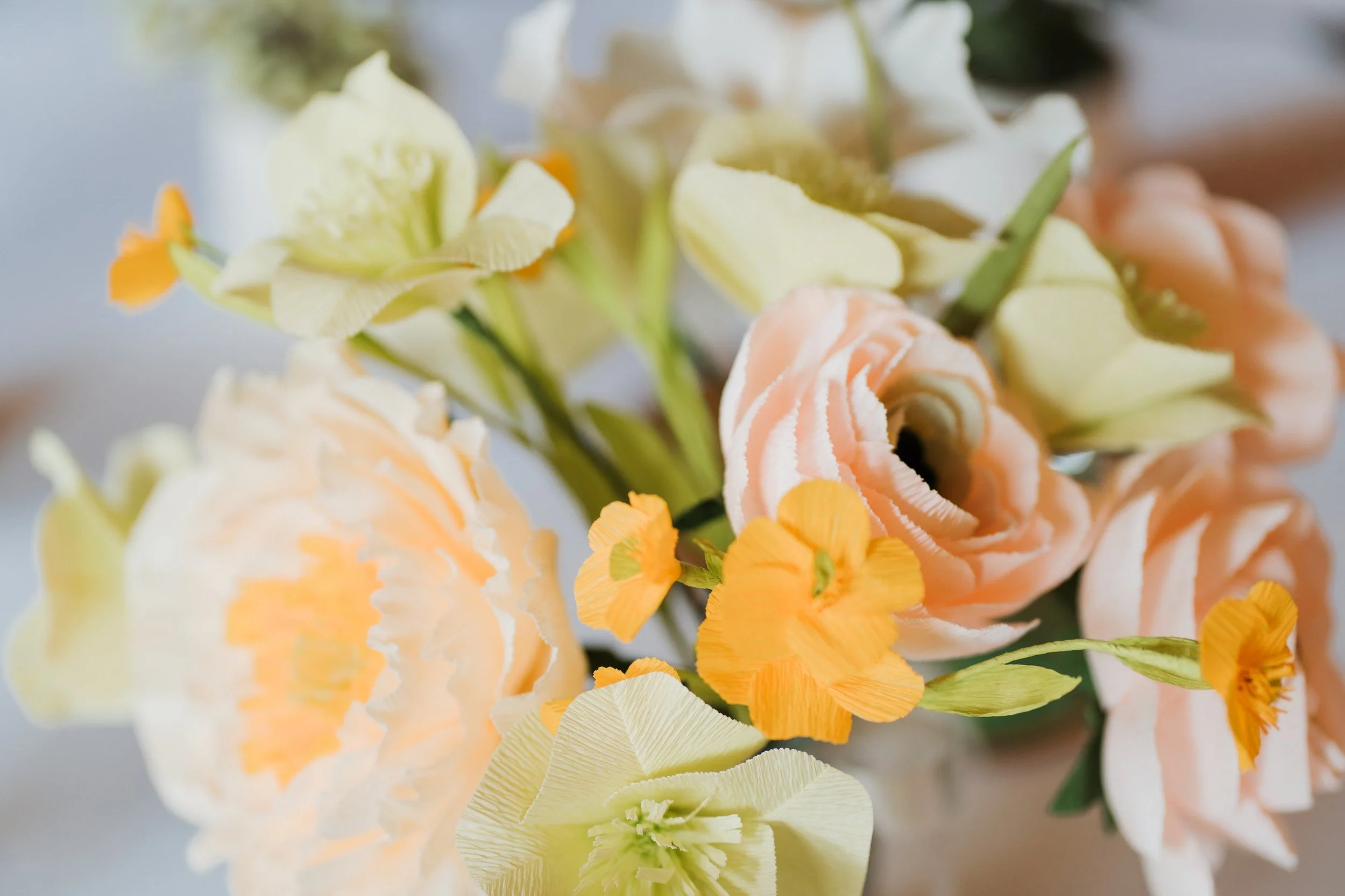 Close-up of a floral arrangement with cream, peach, and yellow flowers, with some small orange flowers interspersed.