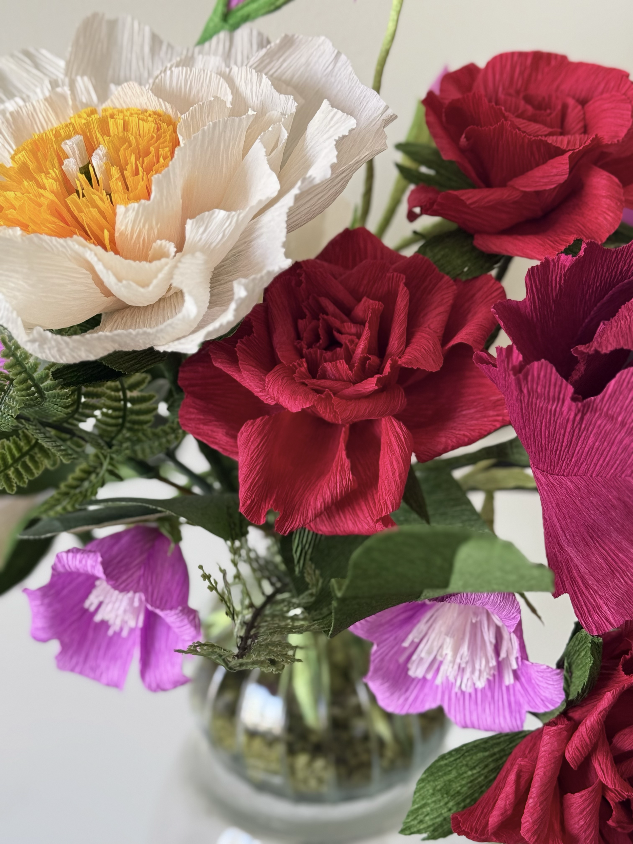 A bouquet of colorful artificial flowers with white, red, purple, and pink petals in a glass vase, with green leaves and stems.
