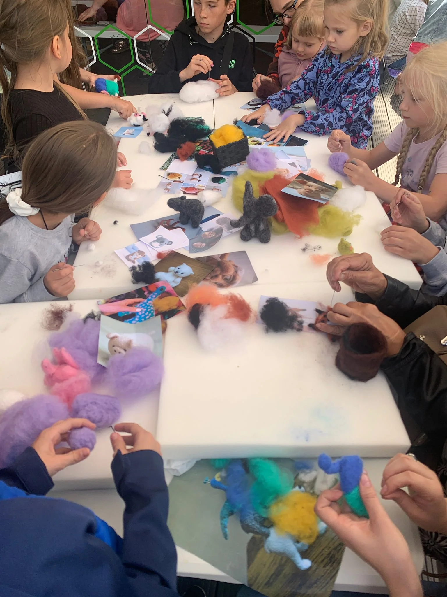 Children engaged in crafting felted animals around a table filled with colorful felted animal projects, photos, and crafting materials.