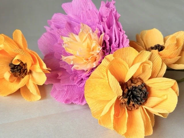 Colorful paper flowers, pink and yellow, arranged on a gray surface.