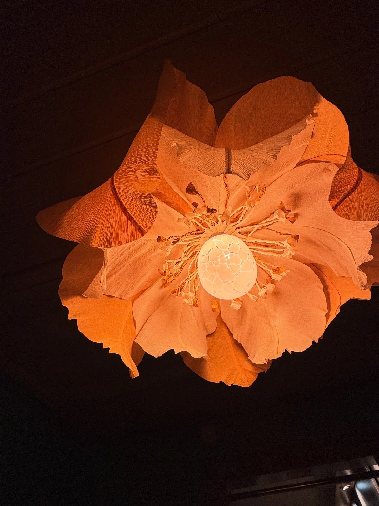 A floral ceiling light fixture resembling a large flower with orange petals and a glowing decorative bulb at the center.