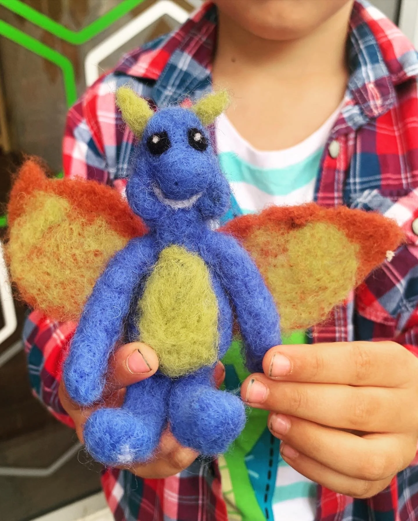 A person holding a colorful felt dragon puppet with blue body, yellow belly, green ears, and orange wings.